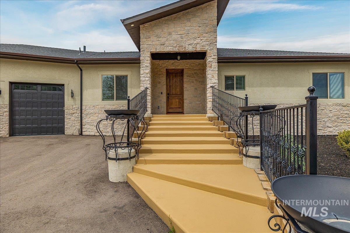Stone and stucco exterior featuring a prominent covered entry, a wood-paneled front door, and a multi-car garage with a paneled door