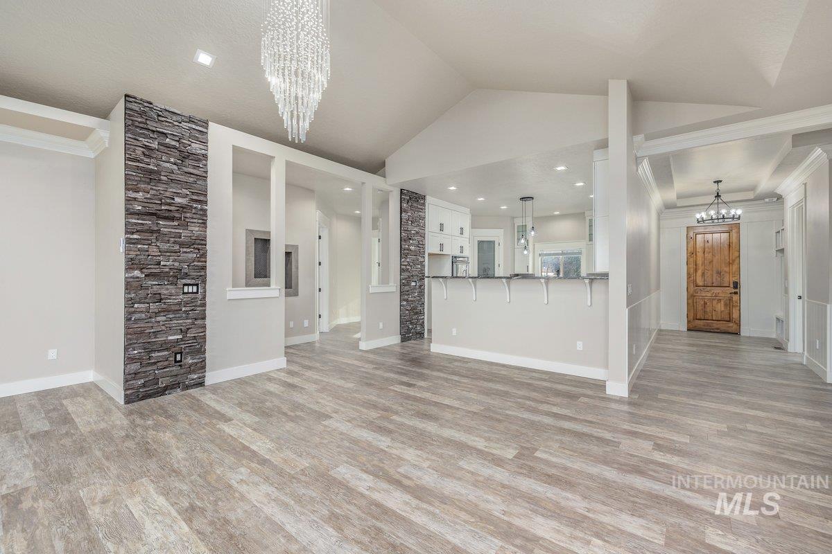 Unfurnished living room featuring a chandelier, light wood-style flooring, vaulted ceiling, and crown molding