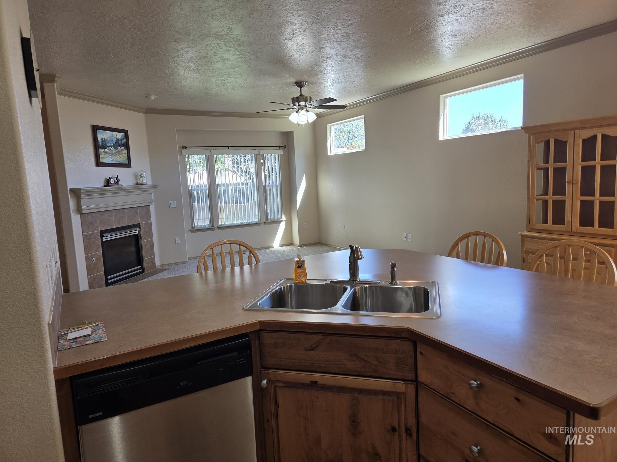 Kitchen with dishwasher, open floor plan, ornamental molding, a tile fireplace, and a textured ceiling