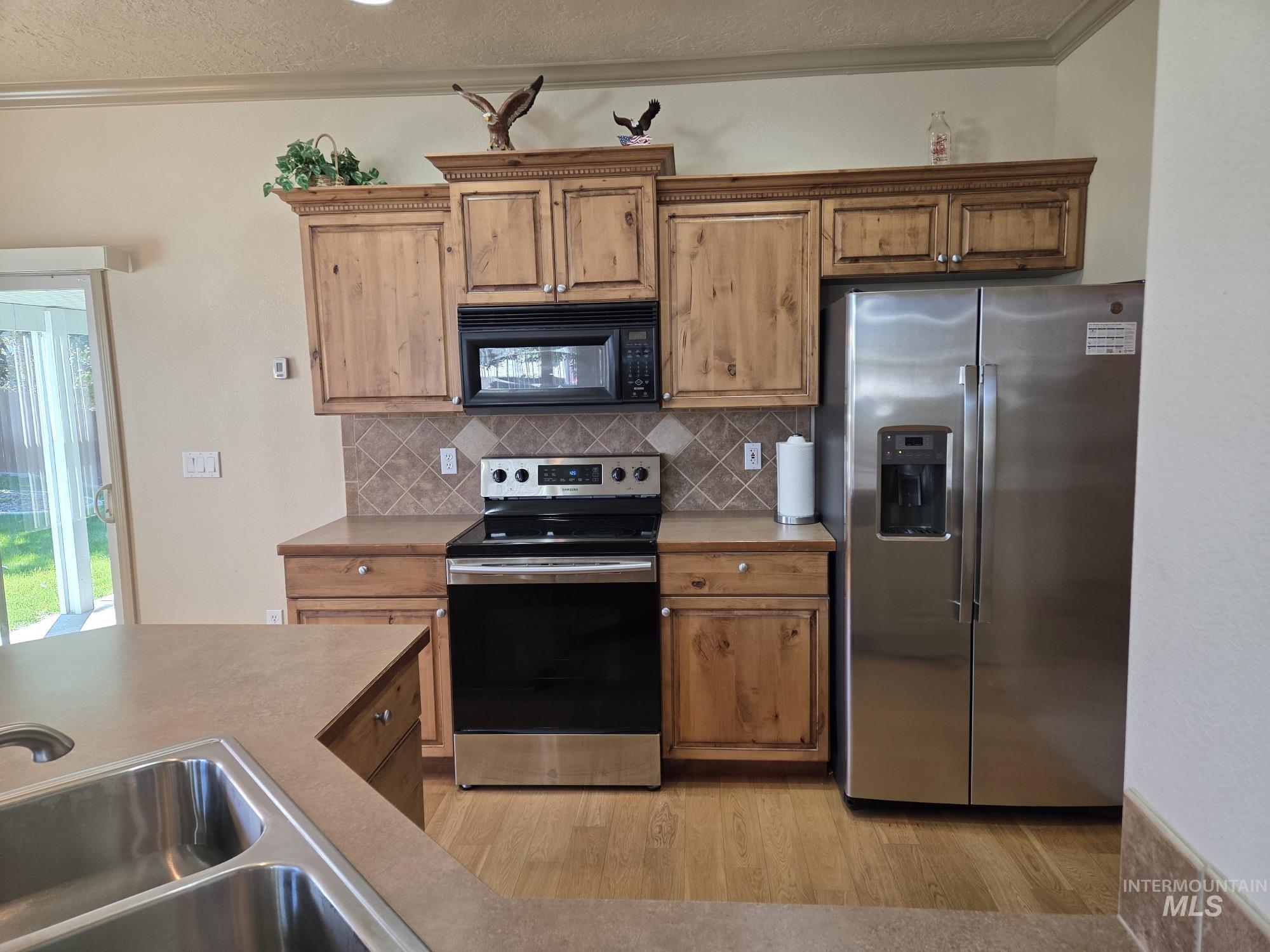 Kitchen featuring appliances with stainless steel finishes, decorative backsplash, ornamental molding, a textured ceiling, and light wood-type flooring
