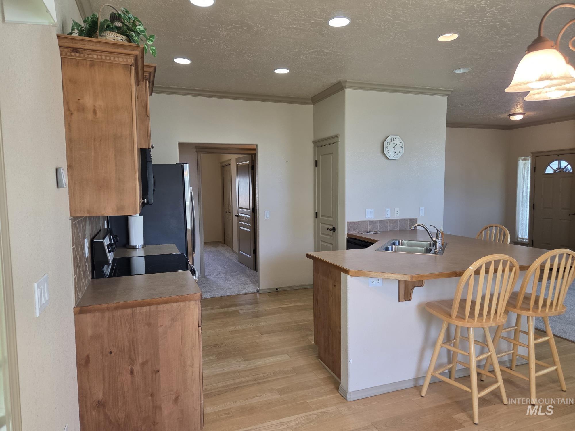 Kitchen with a kitchen breakfast bar, a textured ceiling, ornamental molding, a peninsula, and appliances with stainless steel finishes
