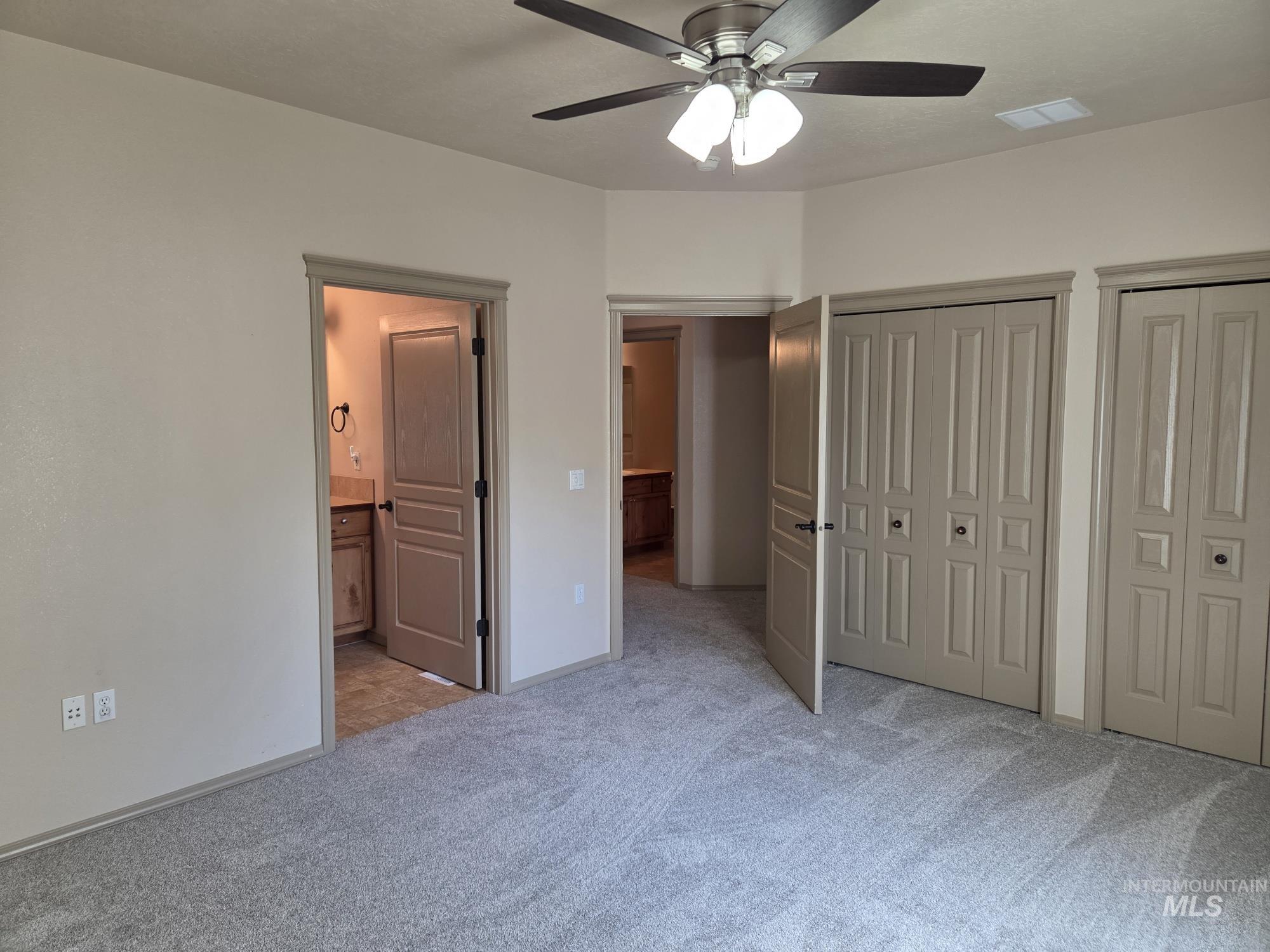 Unfurnished bedroom with multiple closets, light carpet, ensuite bathroom, and a ceiling fan
