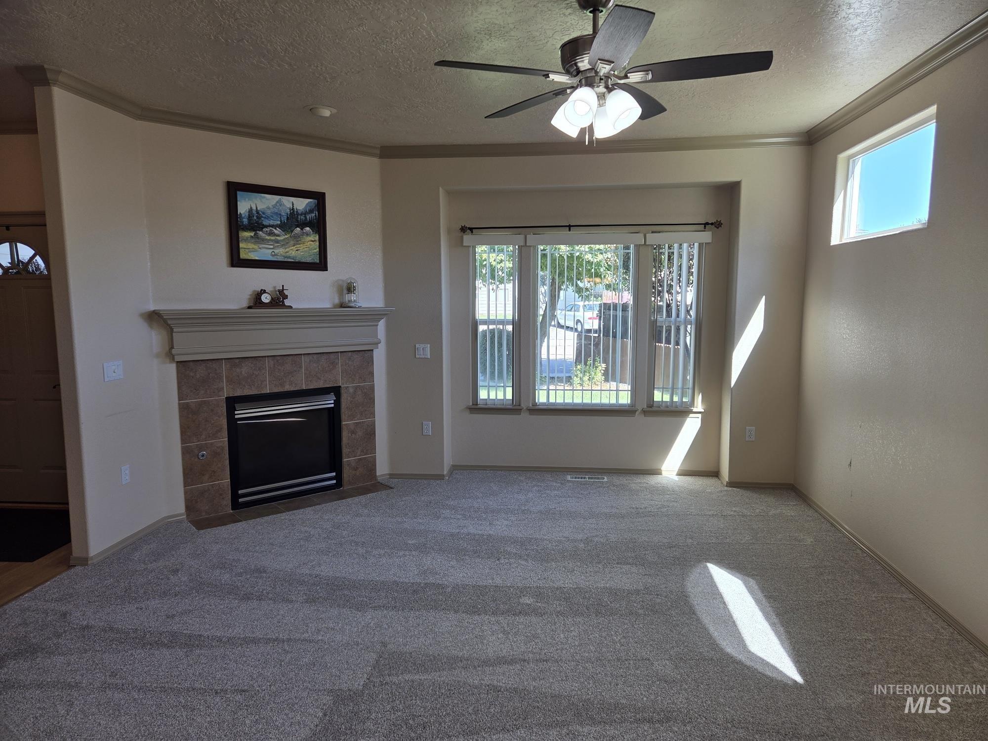 Unfurnished living room featuring crown molding, a textured ceiling, a tile fireplace, carpet flooring, and ceiling fan