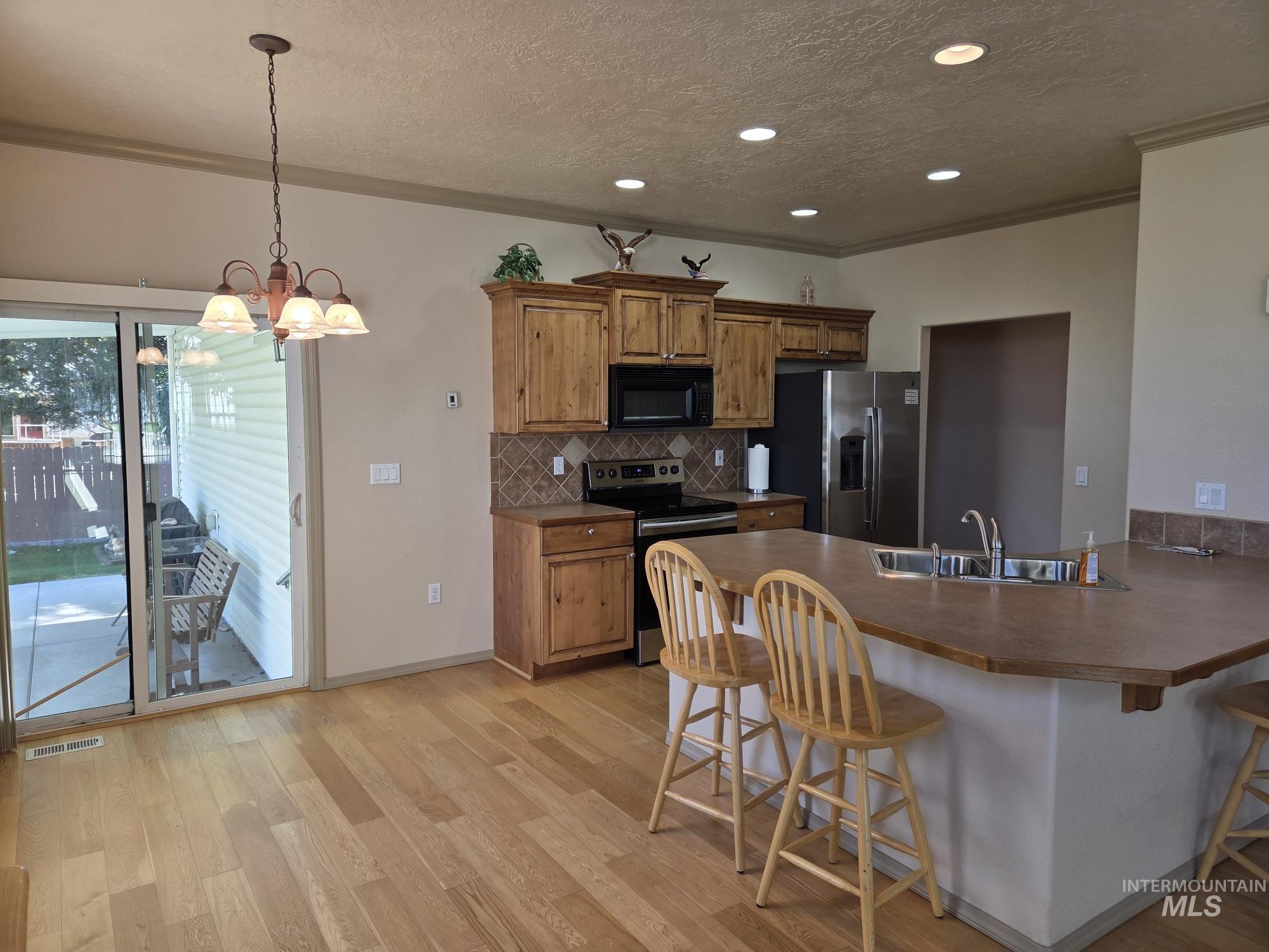 Kitchen with a breakfast bar area, a textured ceiling, backsplash, stainless steel appliances, and a peninsula