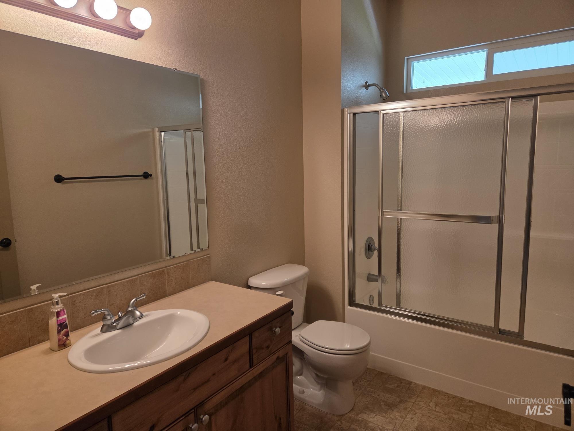 Full bath featuring combined bath / shower with glass door, vanity, and a textured wall