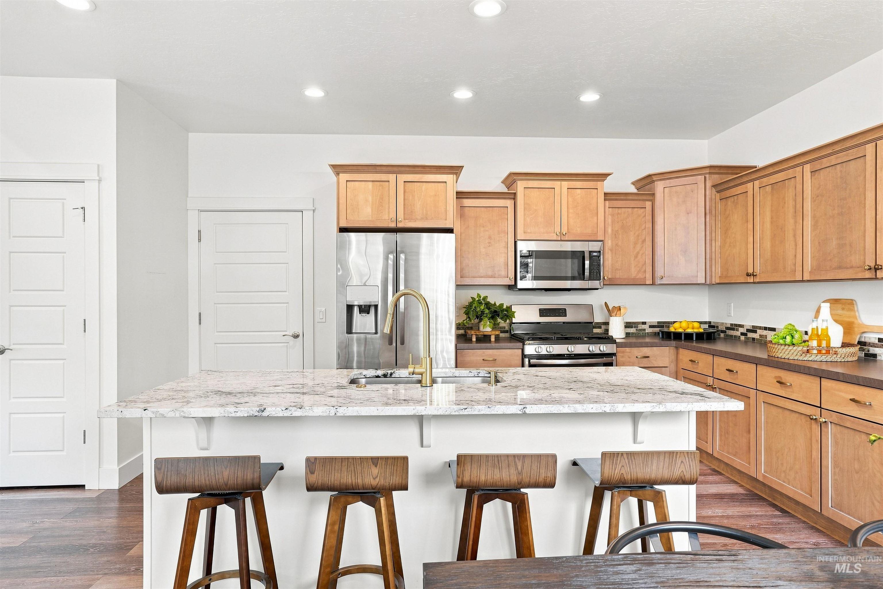 Spacious kitchen featuring an expansive island with an undermount sink, stainless steel appliances, abundant cabinetry, wood-finish flooring, and recessed lighting