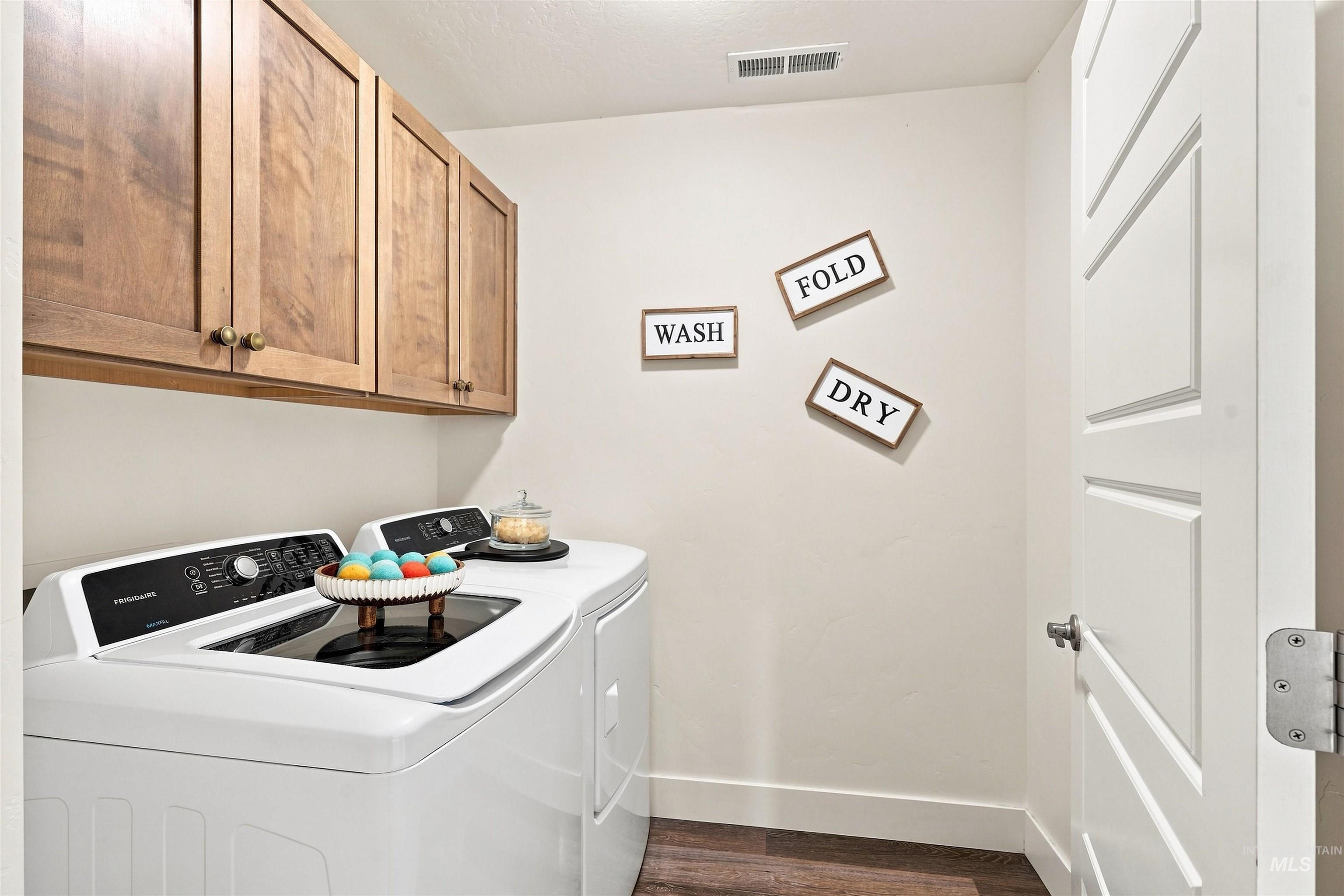 Laundry room featuring wood-finish flooring, white walls, and wood cabinetry with brass hardware