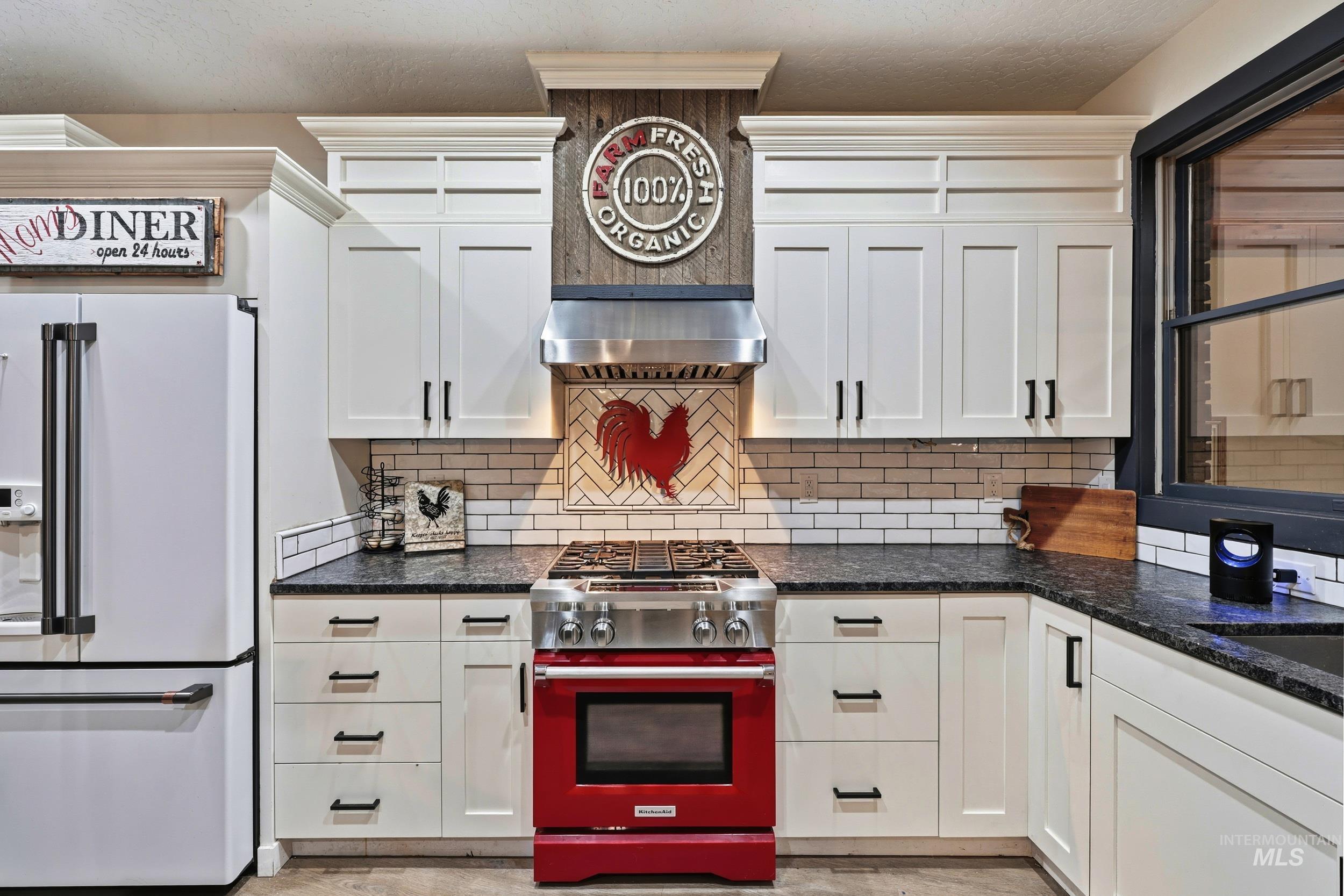 Kitchen featuring high end appliances, white cabinetry, decorative backsplash, and dark stone countertops