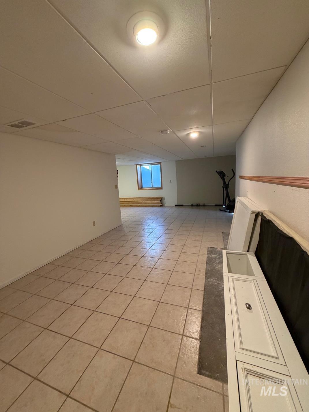 Empty room featuring light tile patterned floors and a drop ceiling