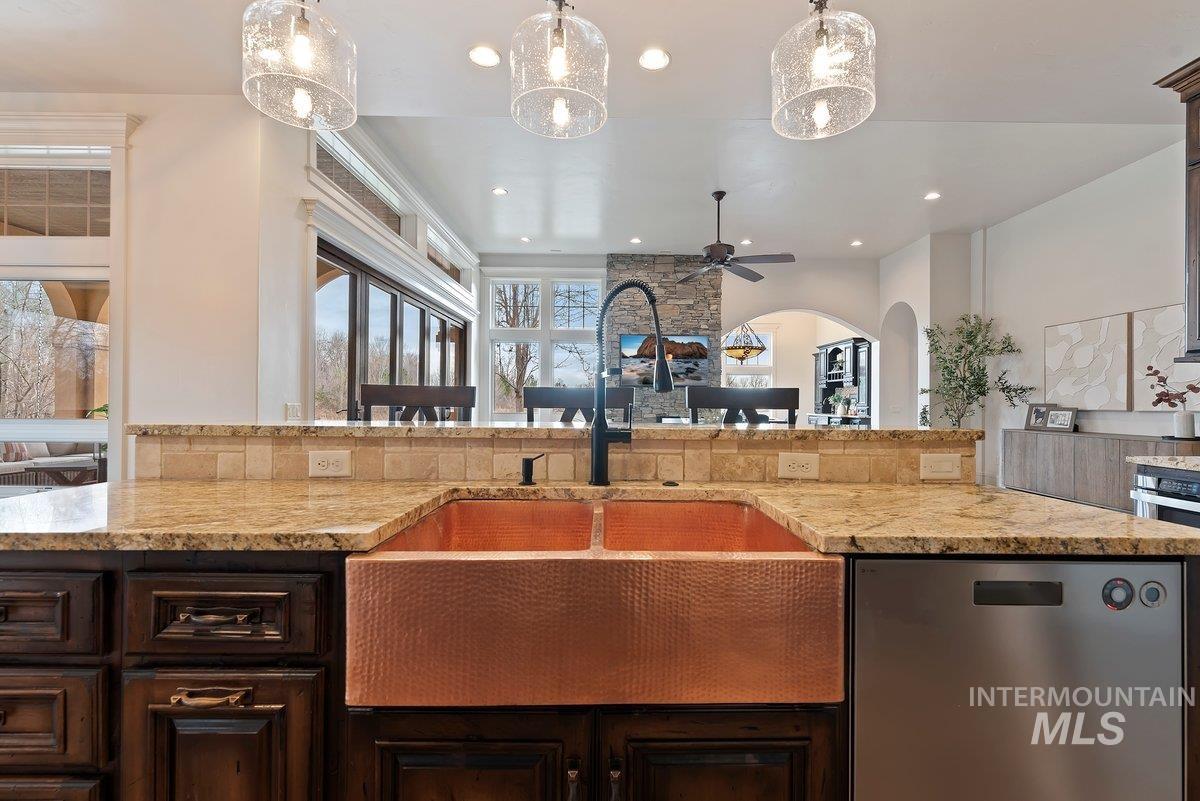 Kitchen featuring dark brown cabinets, stainless steel appliances, light stone counters, hanging light fixtures, and ceiling fan