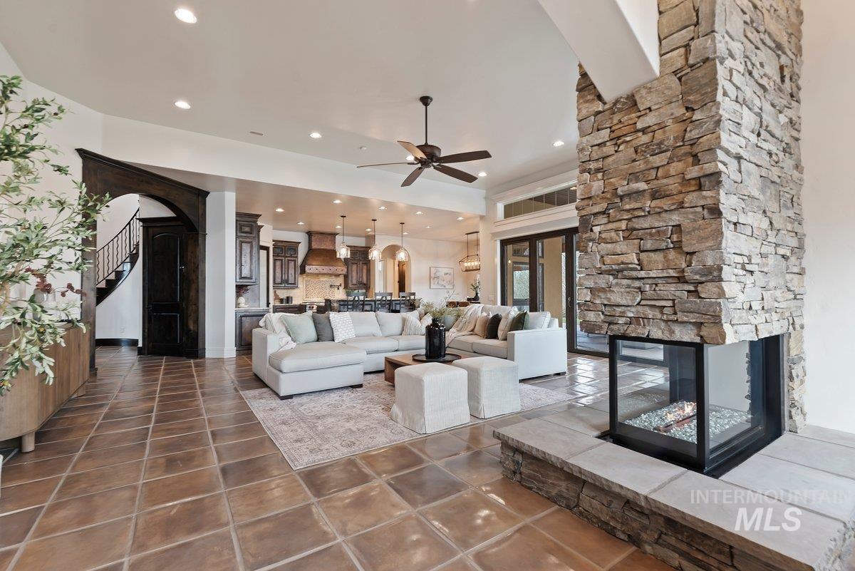 Living area featuring arched walkways, a fireplace, ceiling fan, stairway, and tile patterned floors