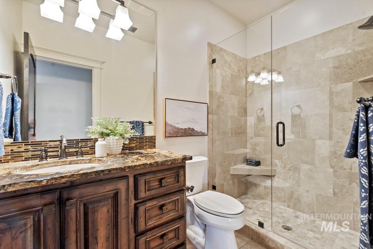 Full bath featuring a shower stall, vanity, and tasteful backsplash