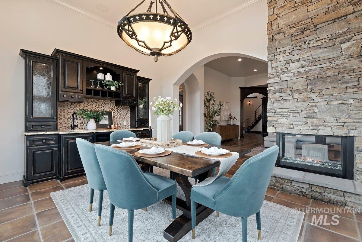 Dining space with arched walkways, dark tile patterned flooring, a stone fireplace, and crown molding