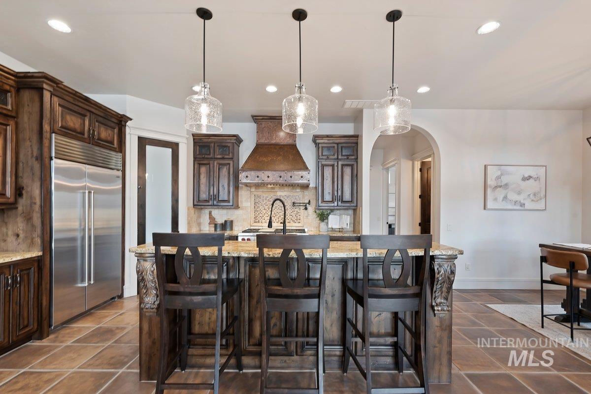 Kitchen featuring dark brown cabinetry, glass insert cabinets, built in refrigerator, light stone counters, and recessed lighting