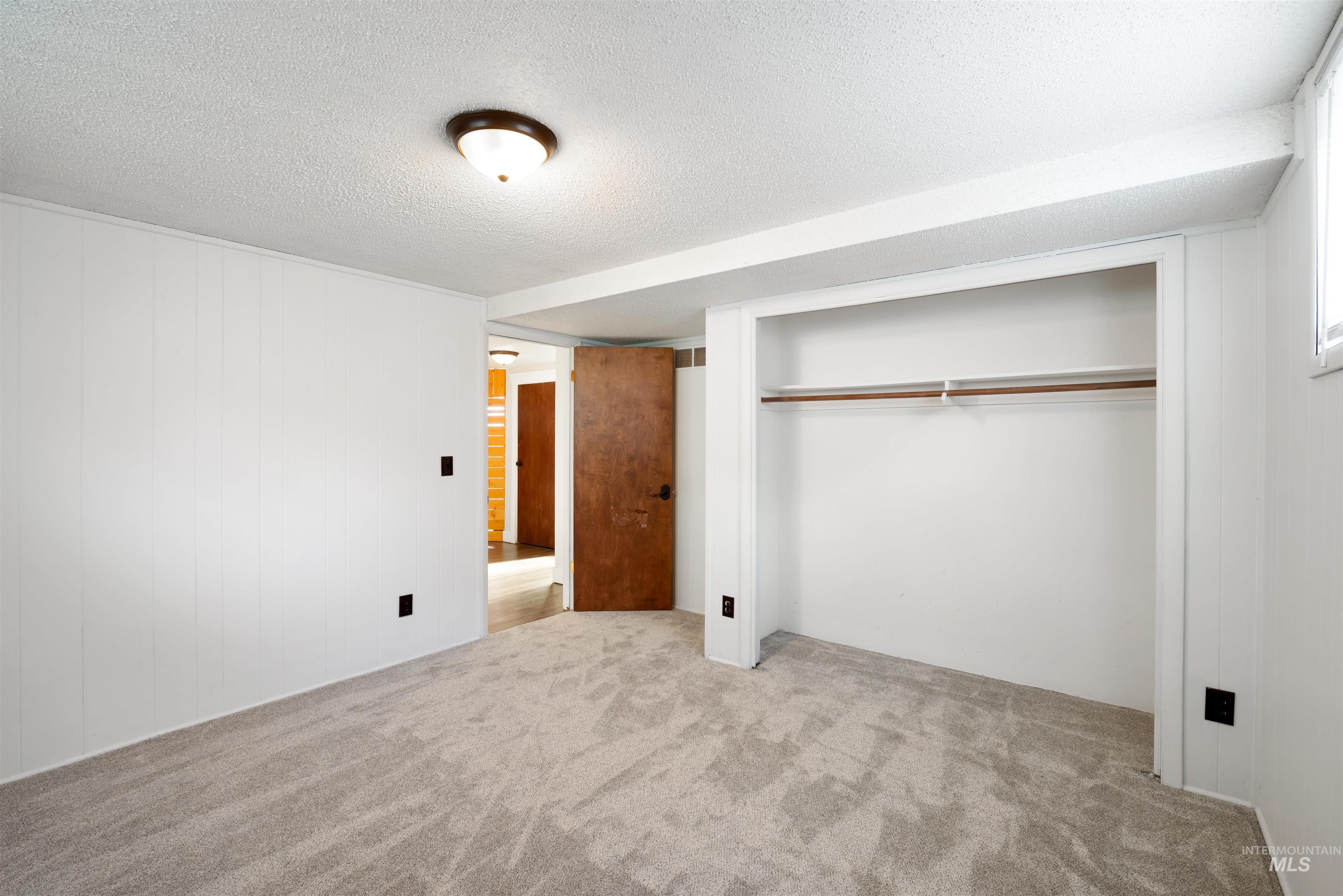 Unfurnished bedroom with carpet, a textured ceiling, a closet, and wooden walls