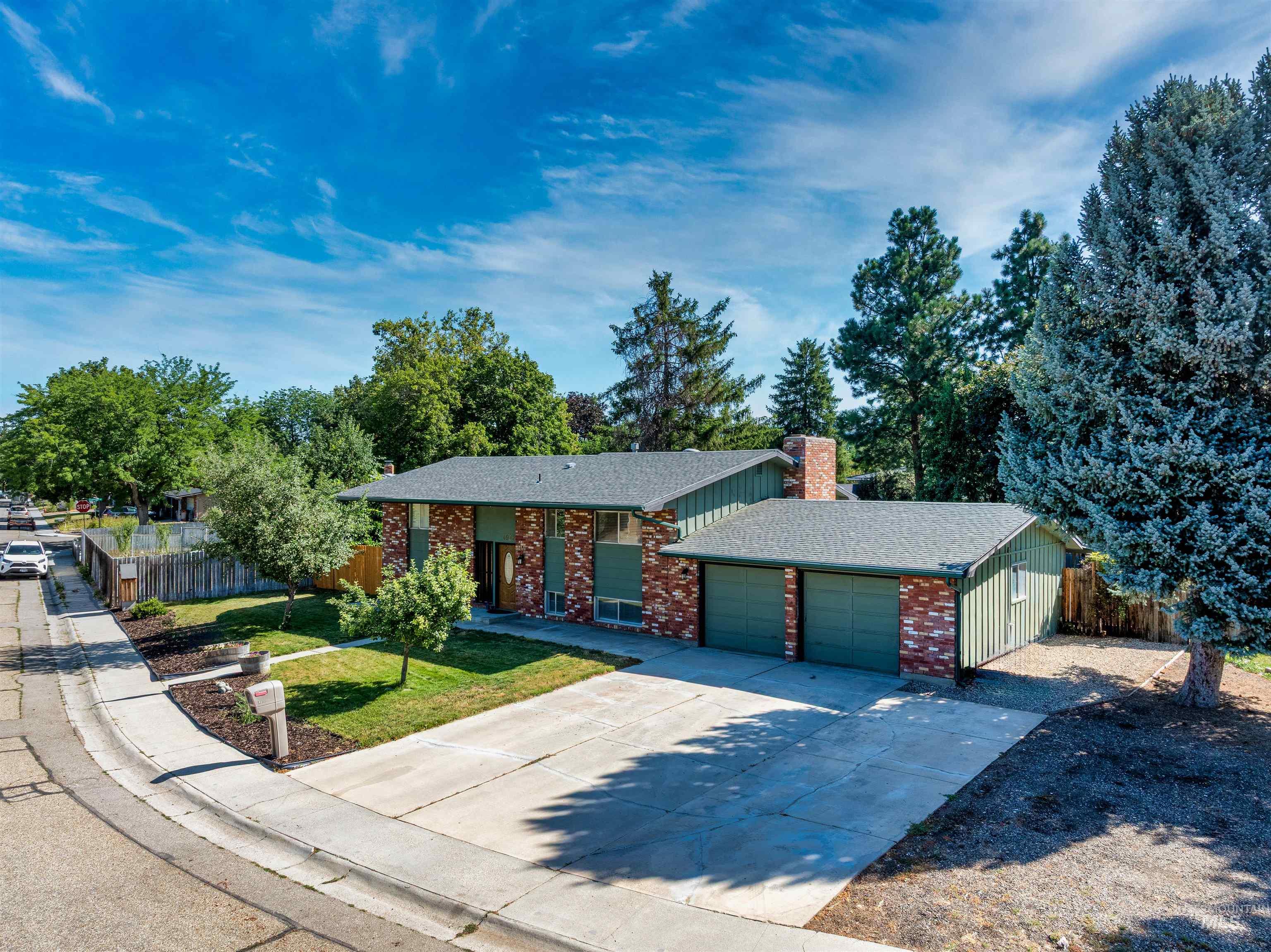 Single story home featuring driveway, brick siding, a chimney, roof with shingles, and a garage