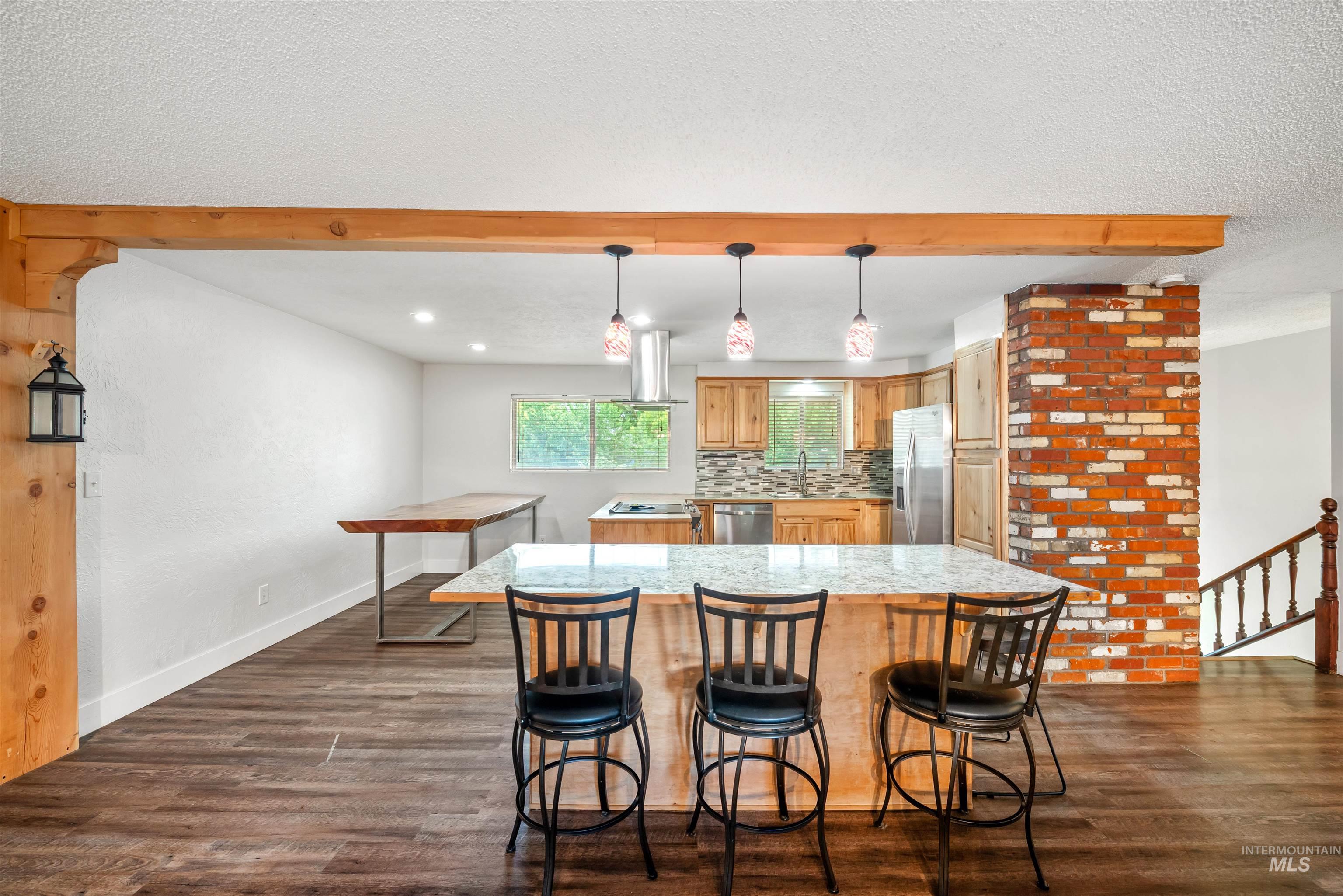 Kitchen featuring a textured ceiling, decorative light fixtures, dark wood-type flooring, backsplash, and a kitchen bar