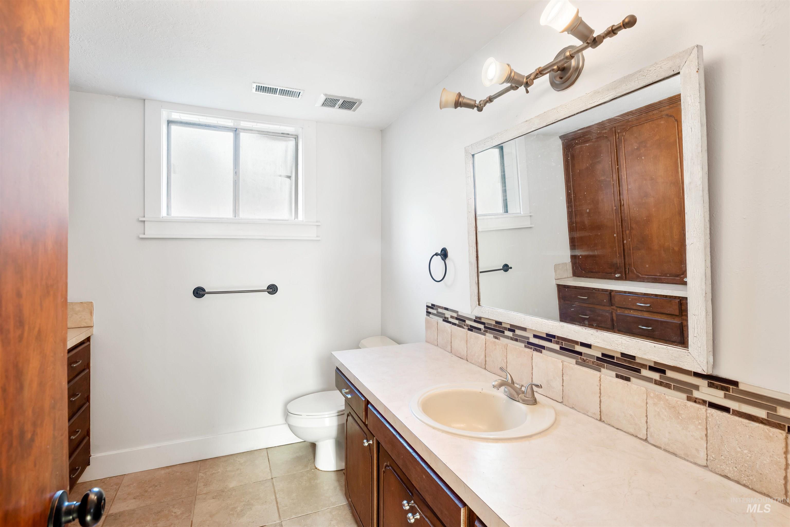 Bathroom with vanity, healthy amount of natural light, light tile patterned flooring, and backsplash