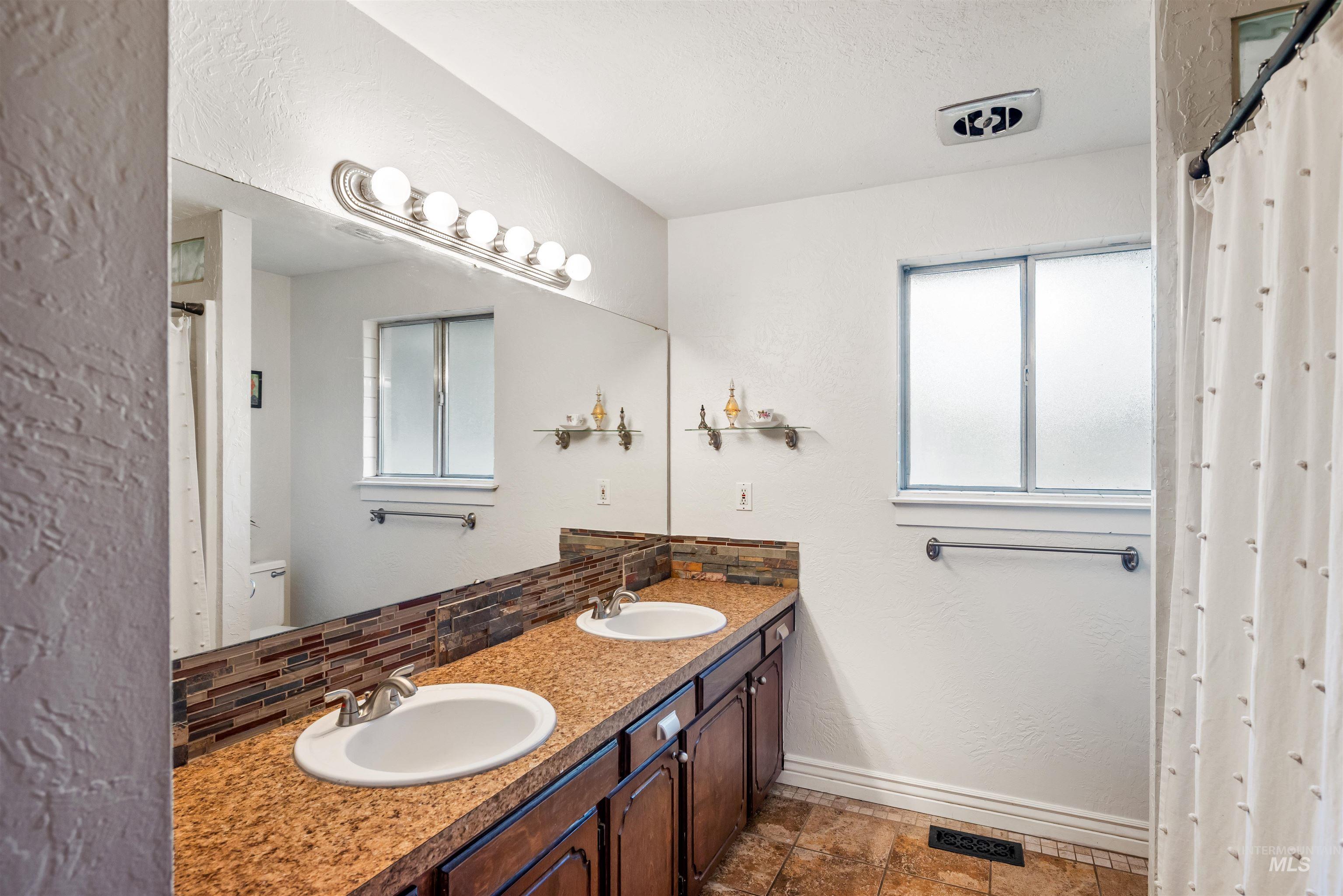 Full bath with a textured wall, double vanity, tasteful backsplash, and a textured ceiling