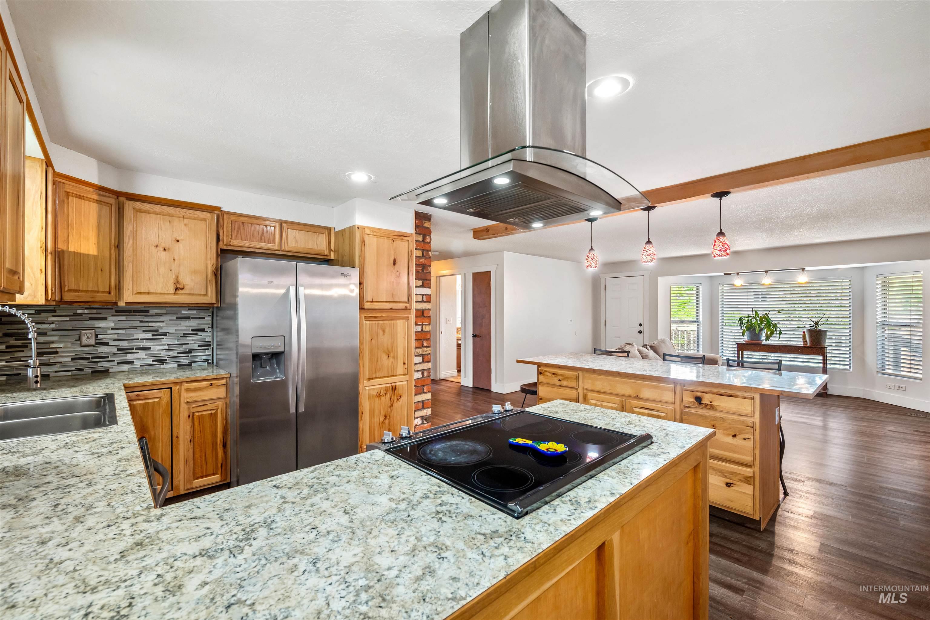 Kitchen featuring island range hood, dark wood-style flooring, stainless steel fridge, decorative light fixtures, and recessed lighting