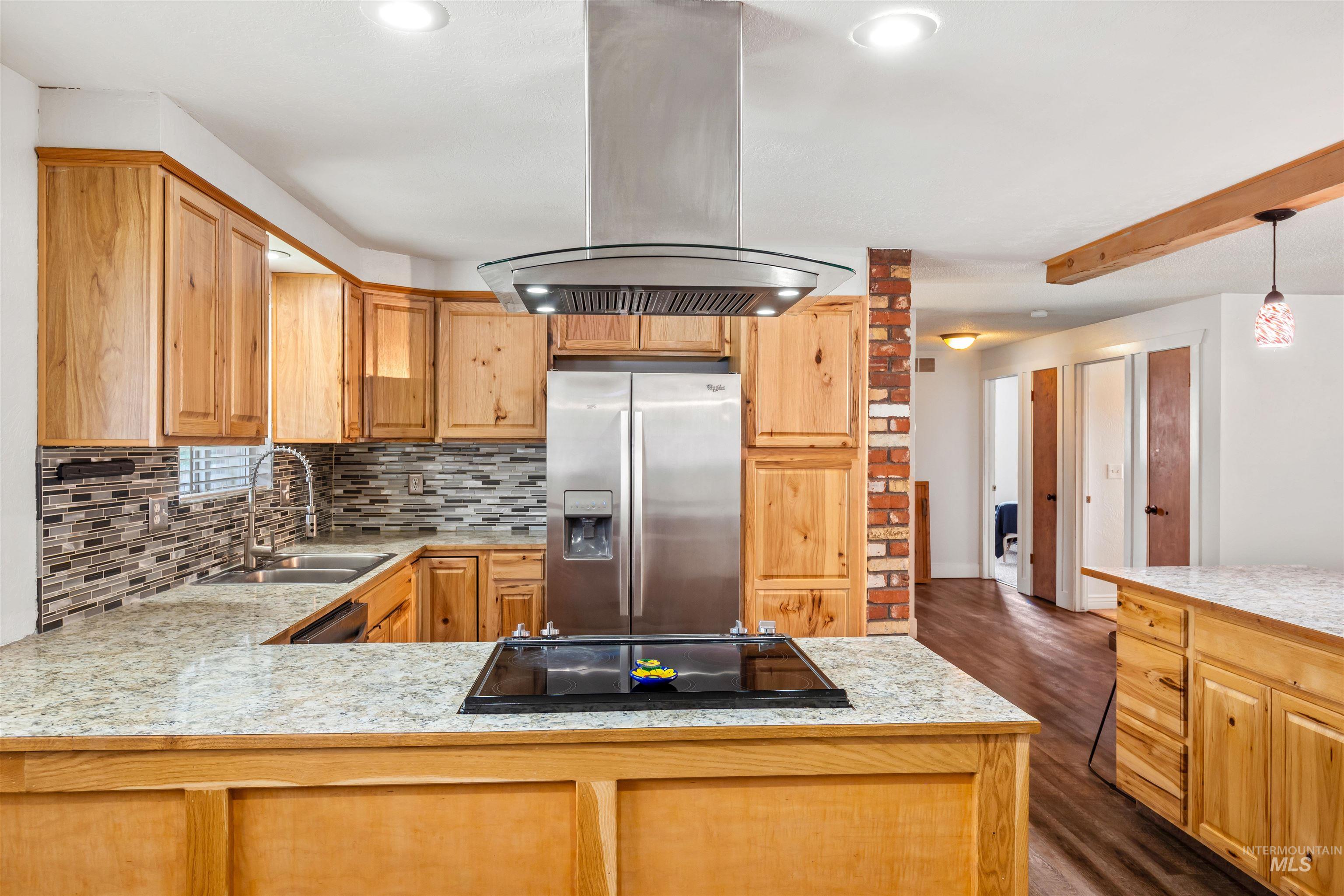 Kitchen featuring light countertops, island range hood, stainless steel refrigerator with ice dispenser, backsplash, and dark wood-type flooring