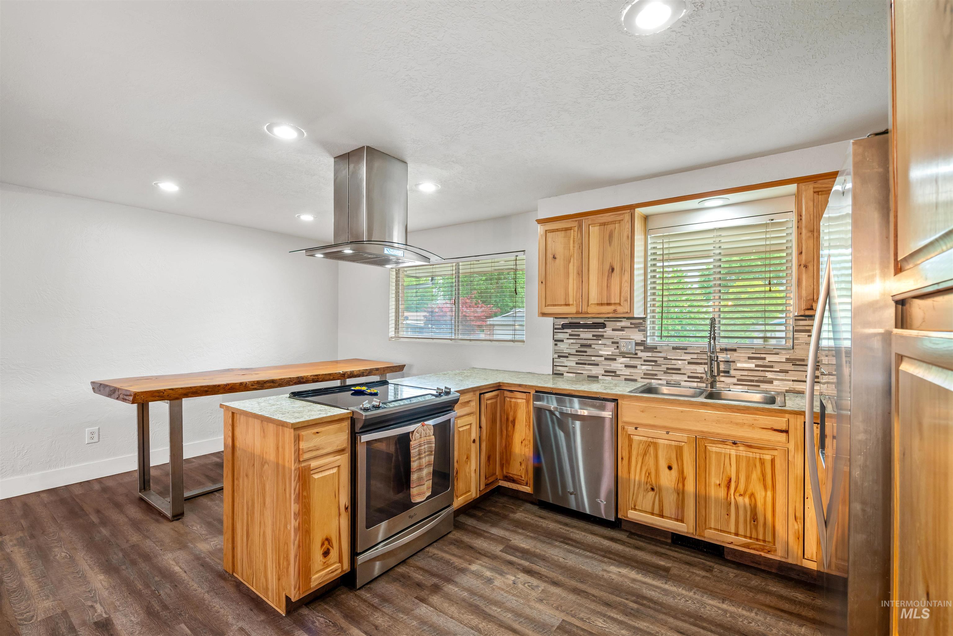 Kitchen with a peninsula, stainless steel appliances, backsplash, island exhaust hood, and recessed lighting