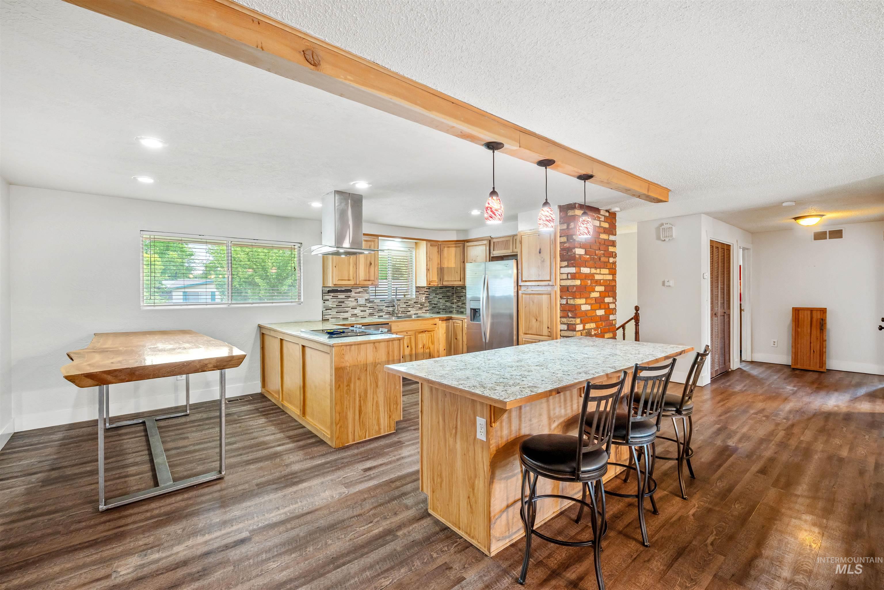 Kitchen with beam ceiling, light countertops, tasteful backsplash, a kitchen breakfast bar, and dark wood-style floors