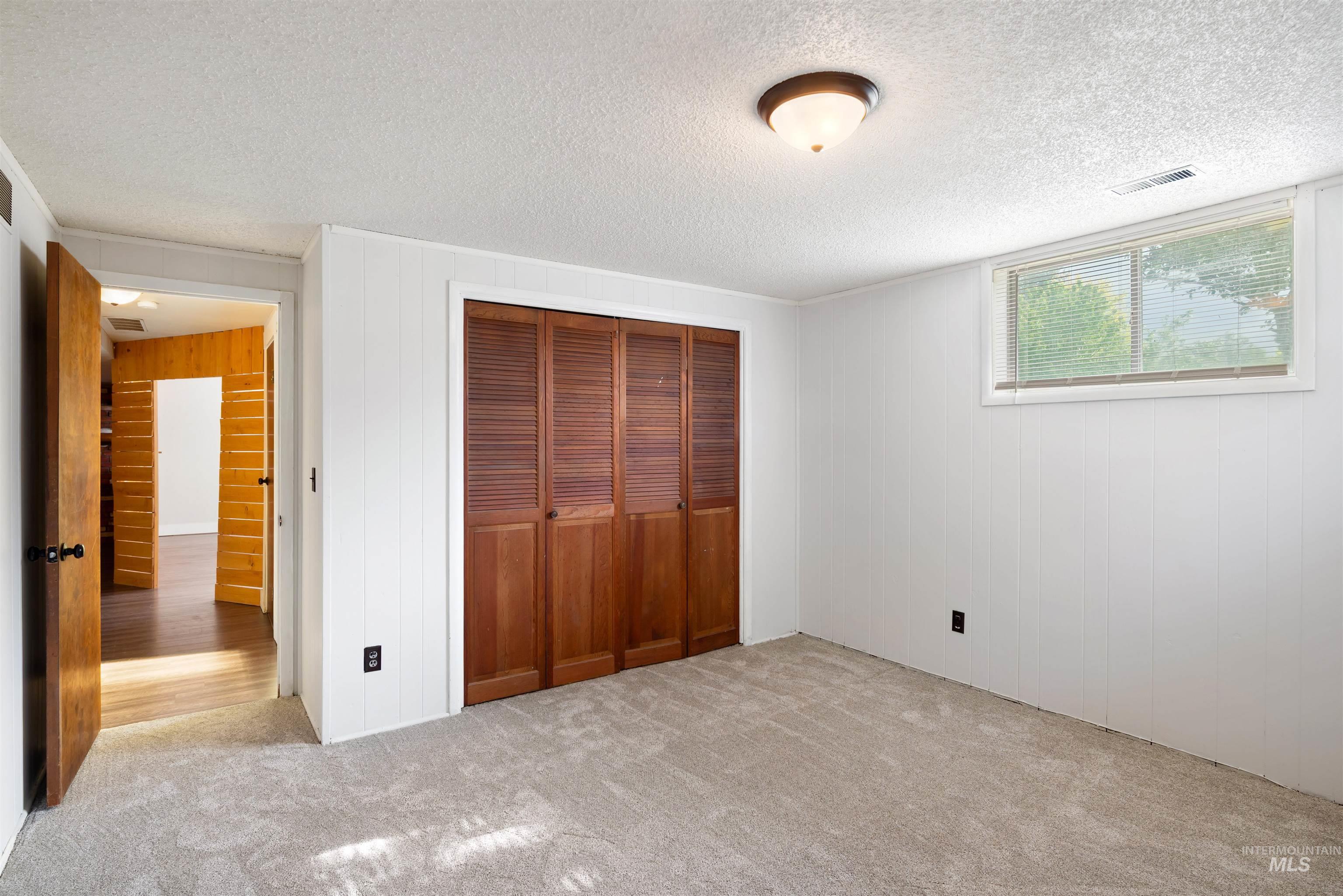 Unfurnished bedroom with carpet, a closet, wooden walls, a textured ceiling, and crown molding