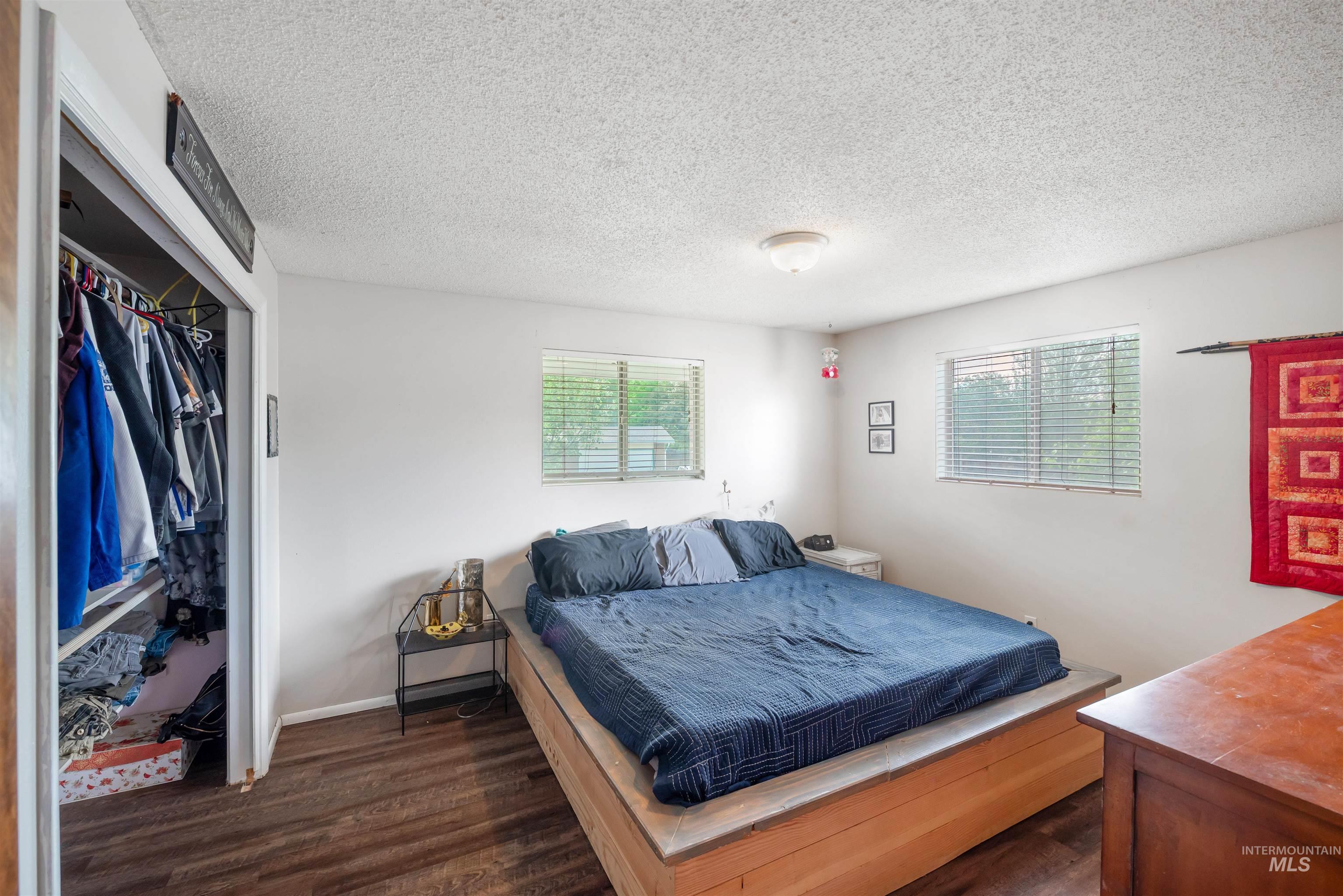 Bedroom with dark wood finished floors, a textured ceiling, and a closet