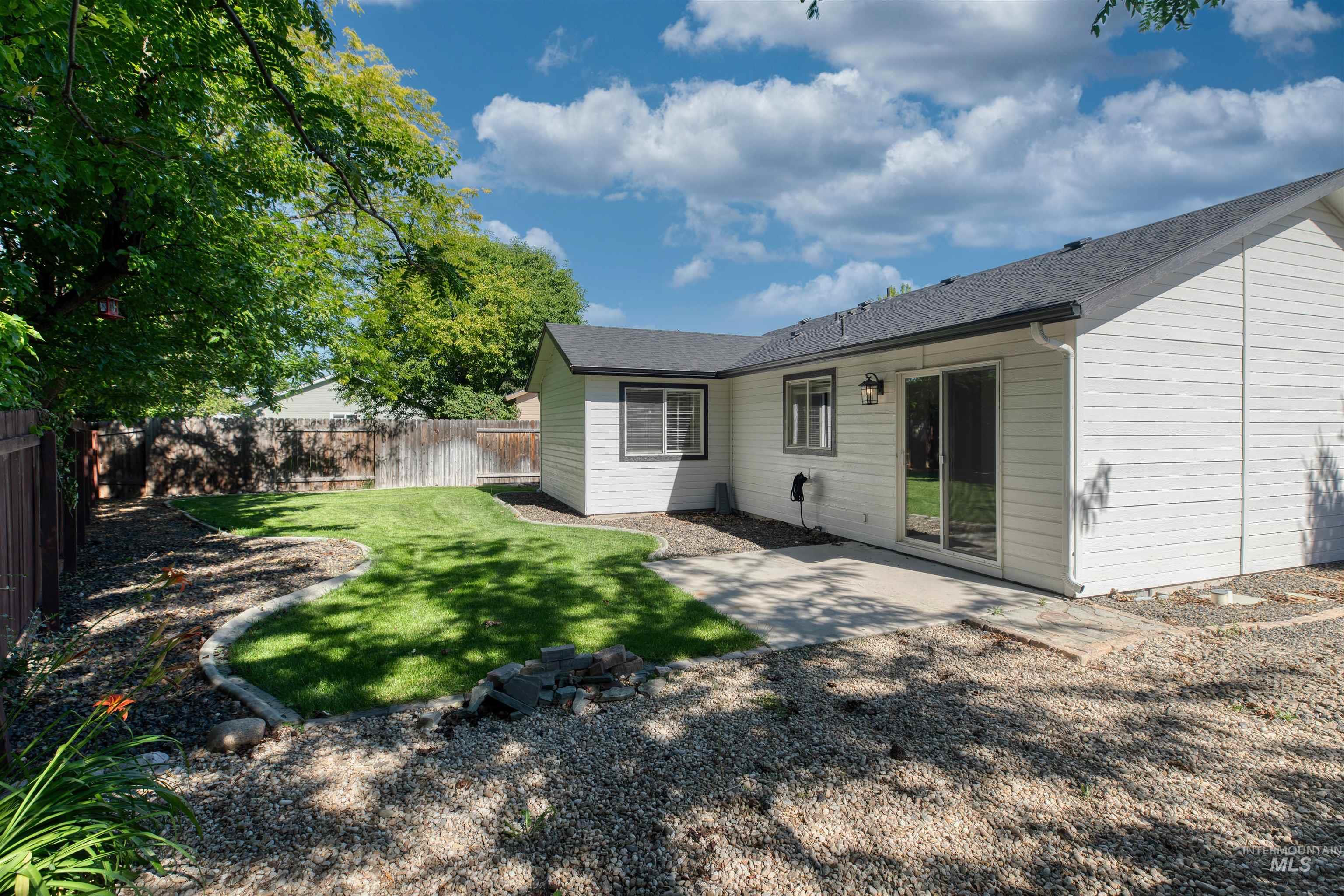 Backyard featuring a concrete patio, sliding glass door access, and a manicured lawn with decorative rock landscaping