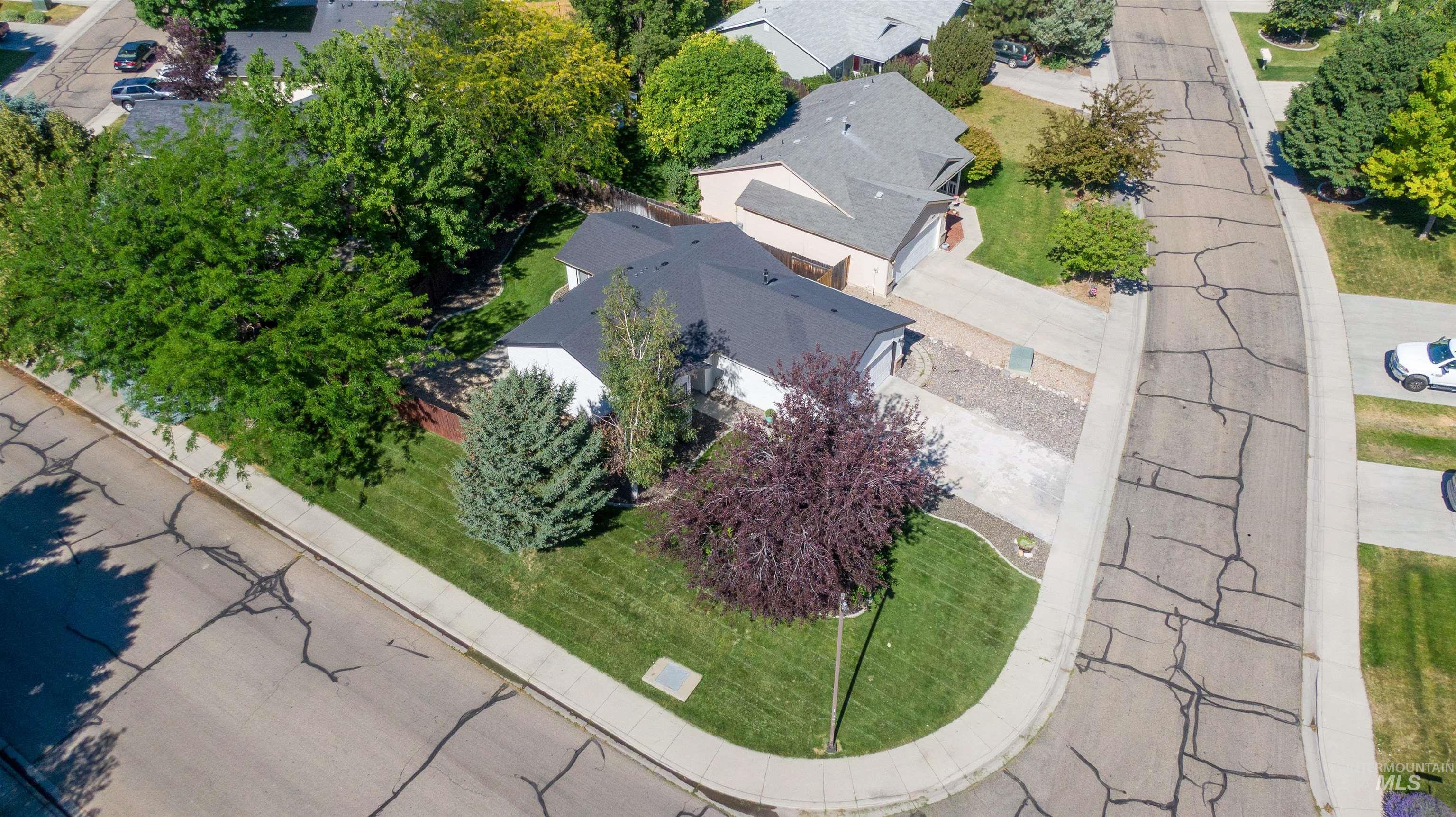 Corner lot property featuring a single-story residence with a dark shingle roof, a manicured lawn, and mature trees