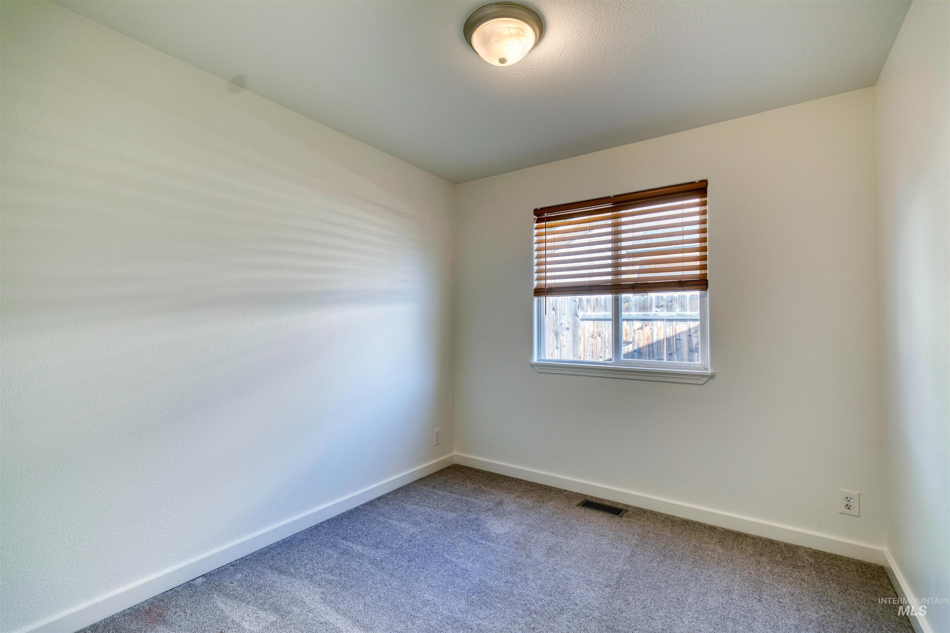 Bedroom featuring light neutral wall paint, gray carpet flooring, a single window with wood-finish blinds, and a flush-mount ceiling light fixture
