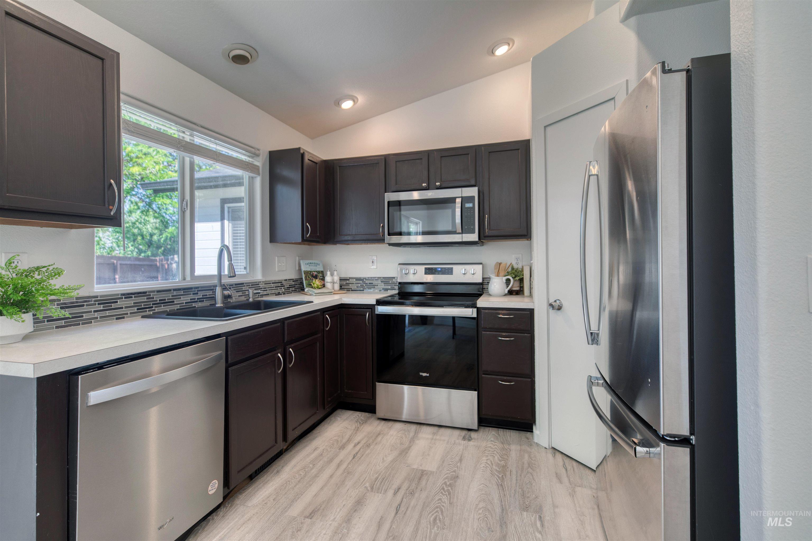 Modern kitchen featuring dark wood-finish cabinetry, stainless steel appliances, light-toned countertops, and a tiled backsplash