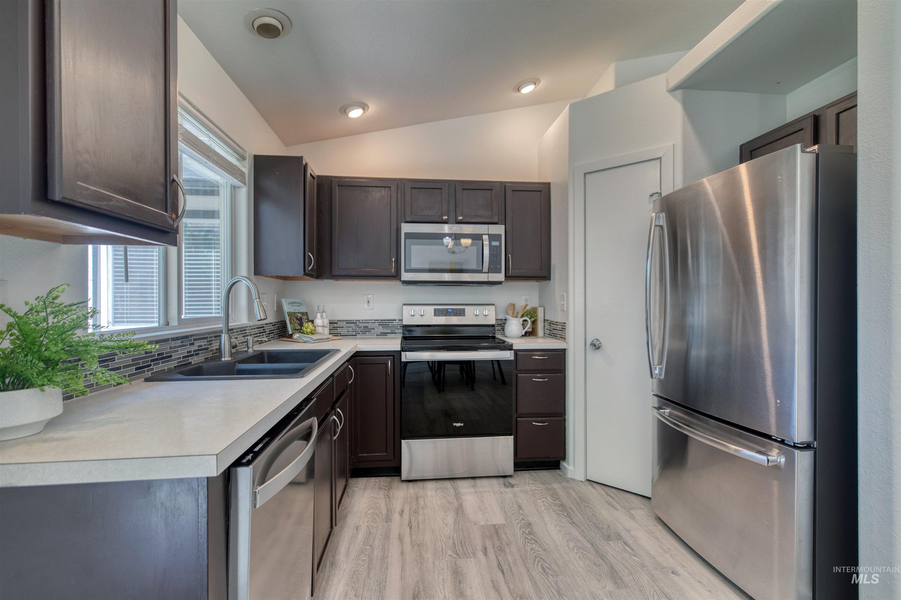 Kitchen featuring dark wood cabinetry, stainless steel appliances, a double basin sink, light-toned countertops, and wood-finish flooring