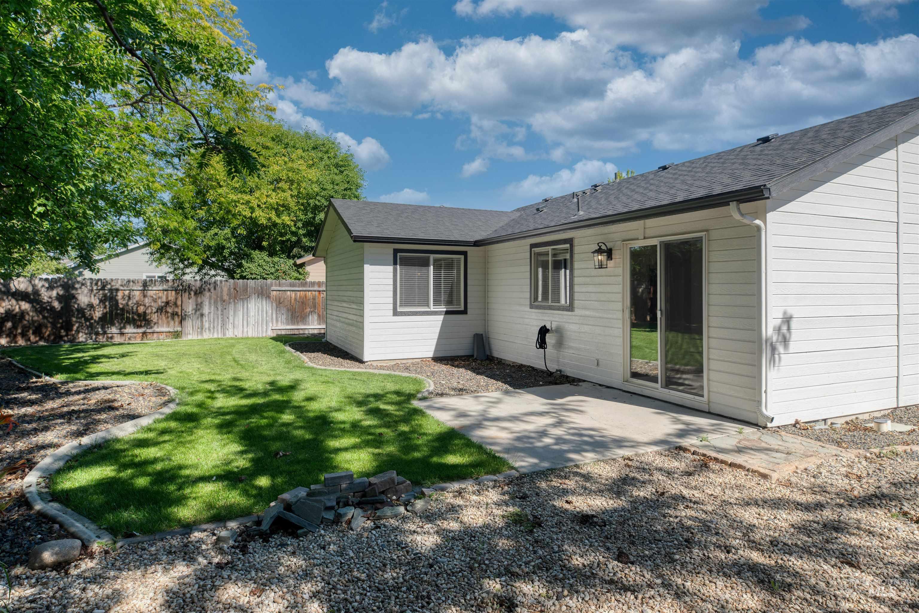 Rear exterior with white siding and dark trim, featuring a concrete patio, sliding glass door, and a manicured lawn area