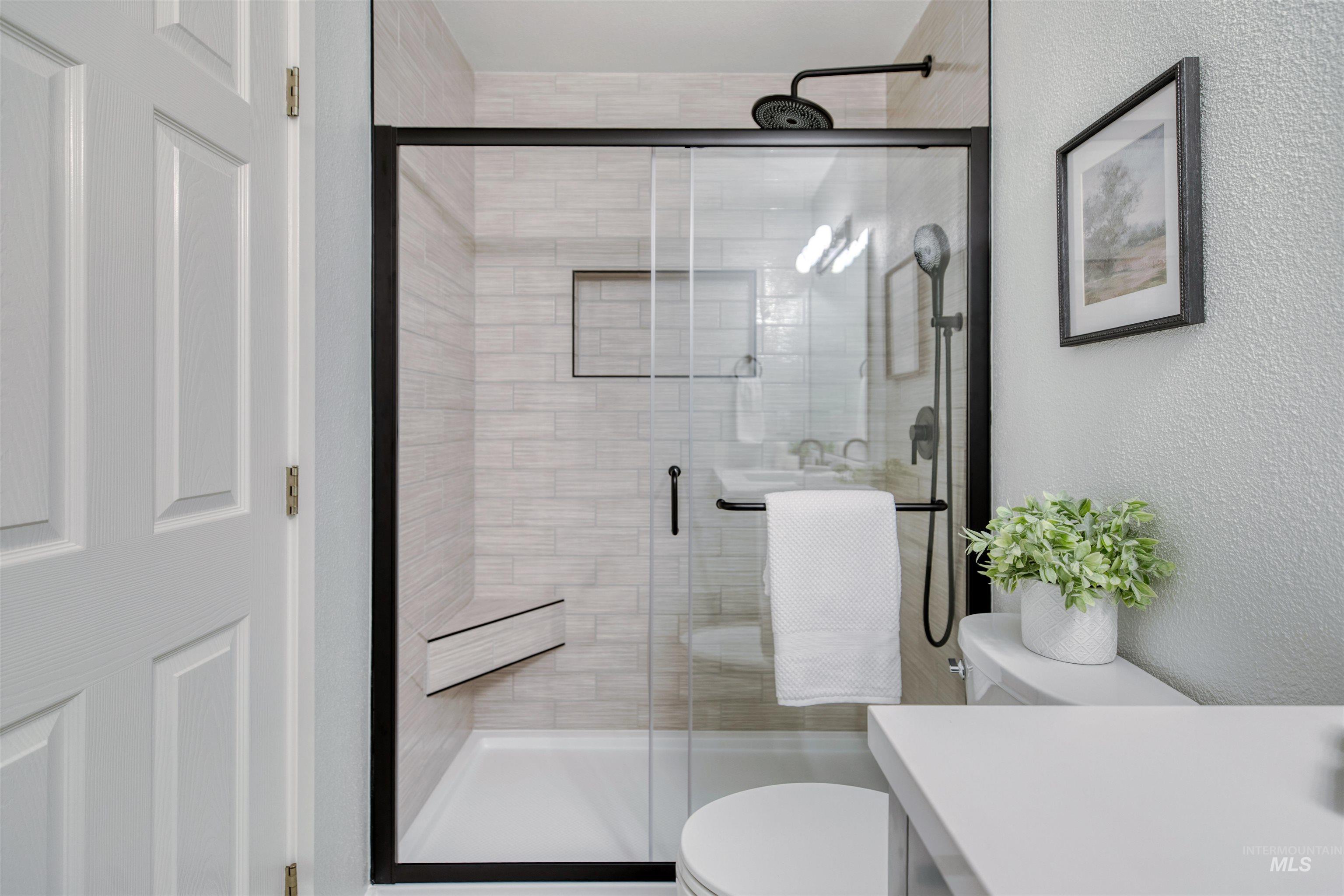 Shower enclosure featuring a black-framed glass door, tiled walls, built-in shower niche, shower bench, and matte black fixtures