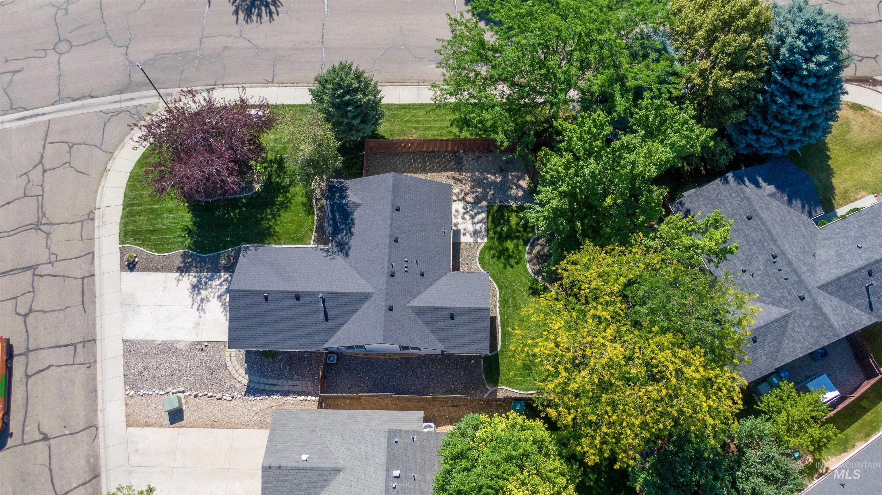 Property featuring a dark shingle roof, mature landscaping, a paved driveway, and rock beds