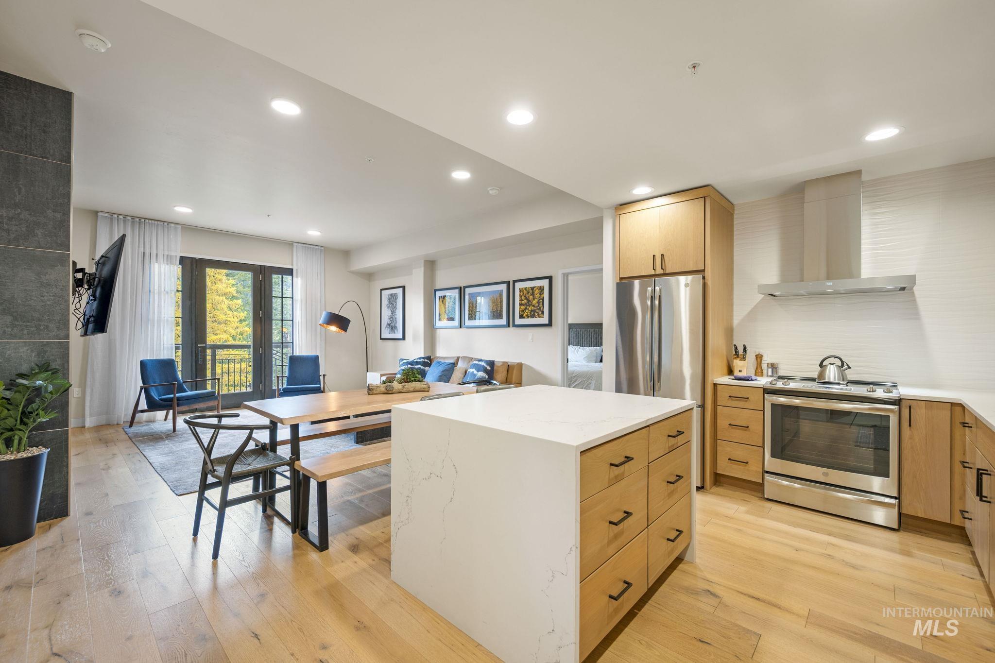 Kitchen with stainless steel electric range oven, wall chimney range hood, recessed lighting, light wood-type flooring, and a kitchen island