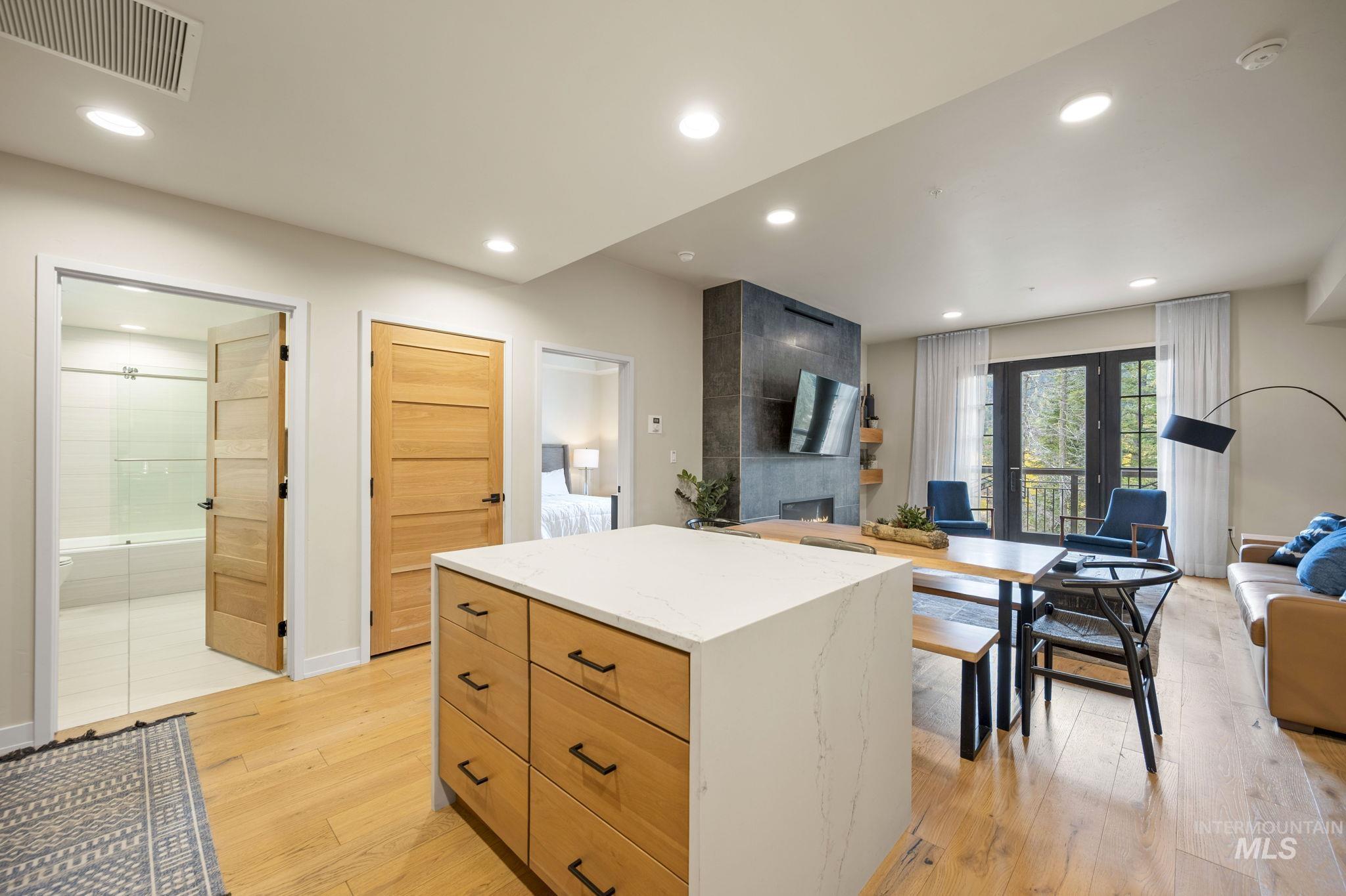 Kitchen with recessed lighting, light wood-style flooring, open floor plan, a tile fireplace, and light stone counters