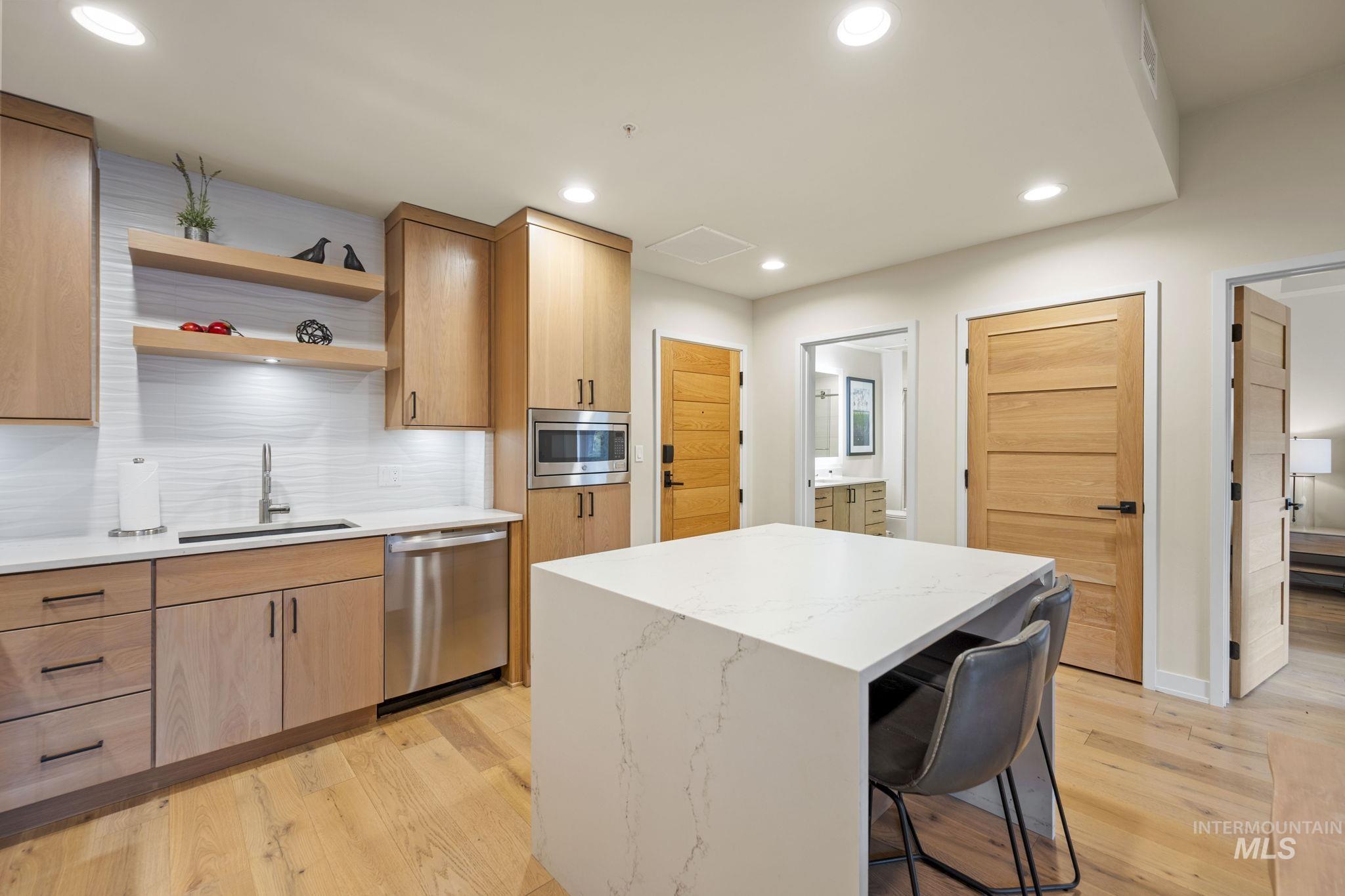 Kitchen featuring light stone countertops, open shelves, decorative backsplash, a kitchen island, and light wood finished floors