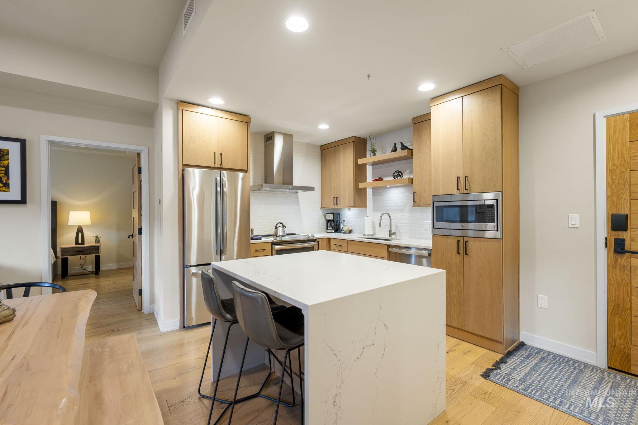 Kitchen featuring open shelves, a kitchen bar, appliances with stainless steel finishes, light stone countertops, and decorative backsplash