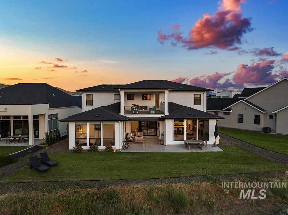 Back of property at dusk featuring a balcony, a patio area, a yard, and stucco siding