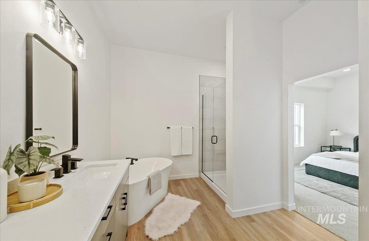 Full bathroom with light wood-type flooring, a shower stall, a soaking tub, vanity, and ensuite bath