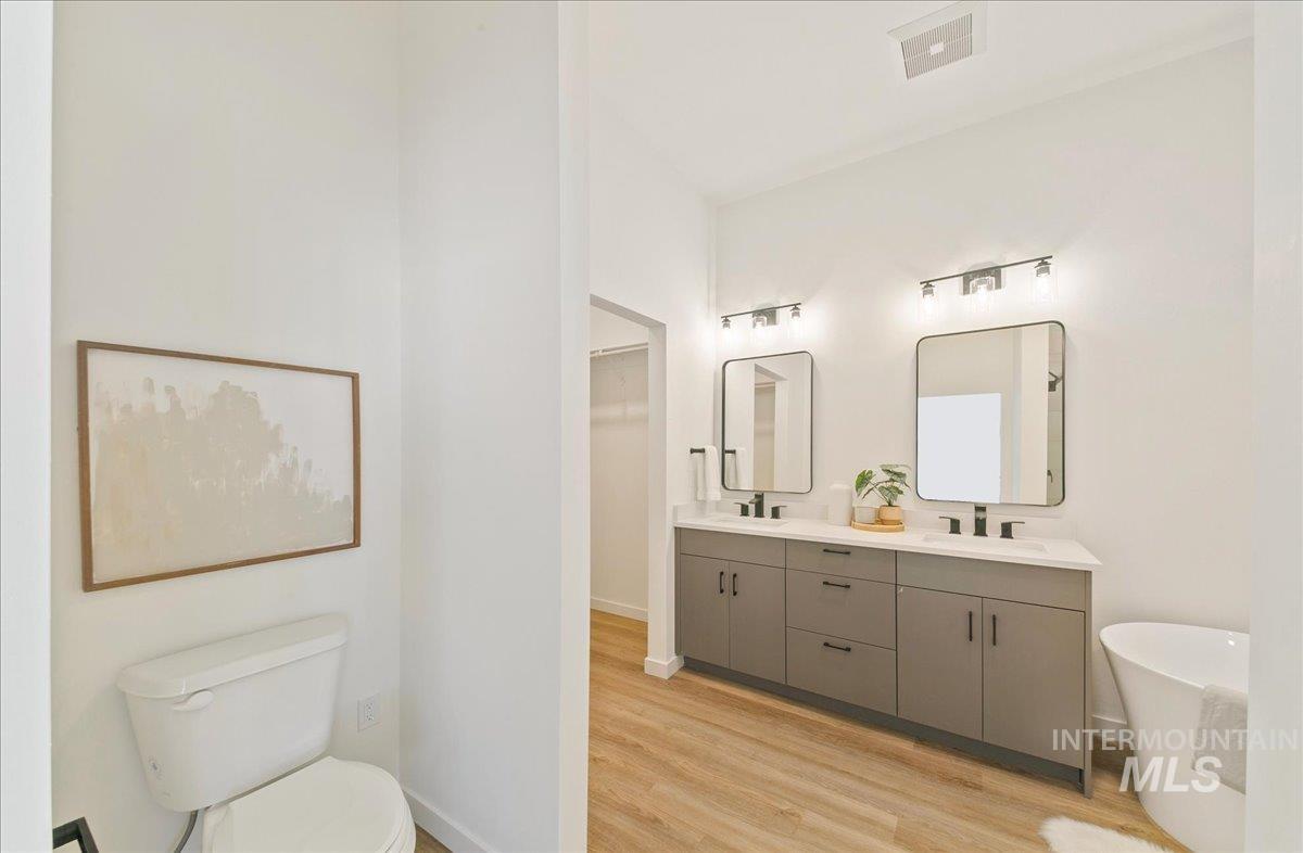 Full bath with a freestanding bath, double vanity, and light wood-style flooring
