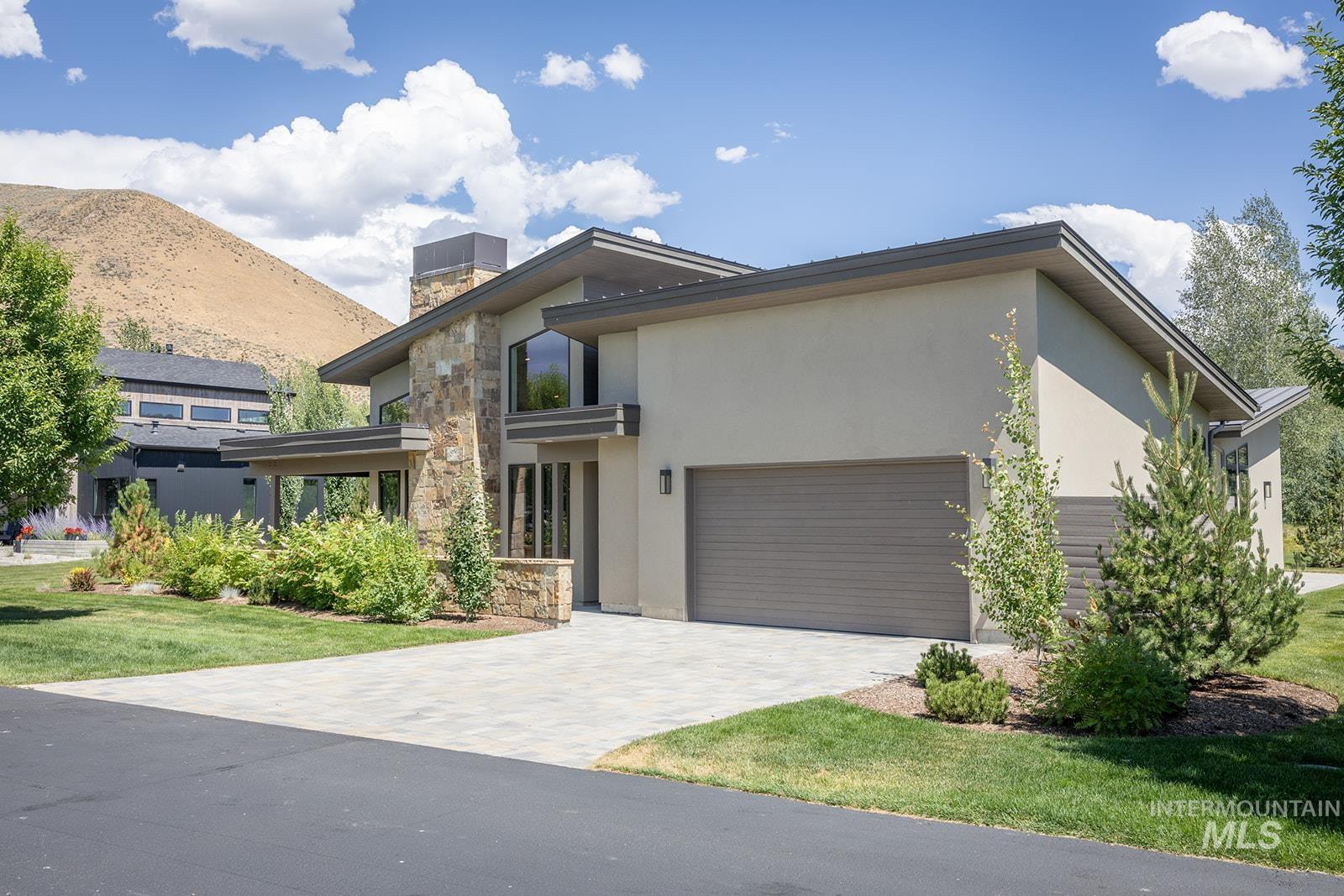 Modern home with stone siding, stucco siding, a garage, and decorative driveway