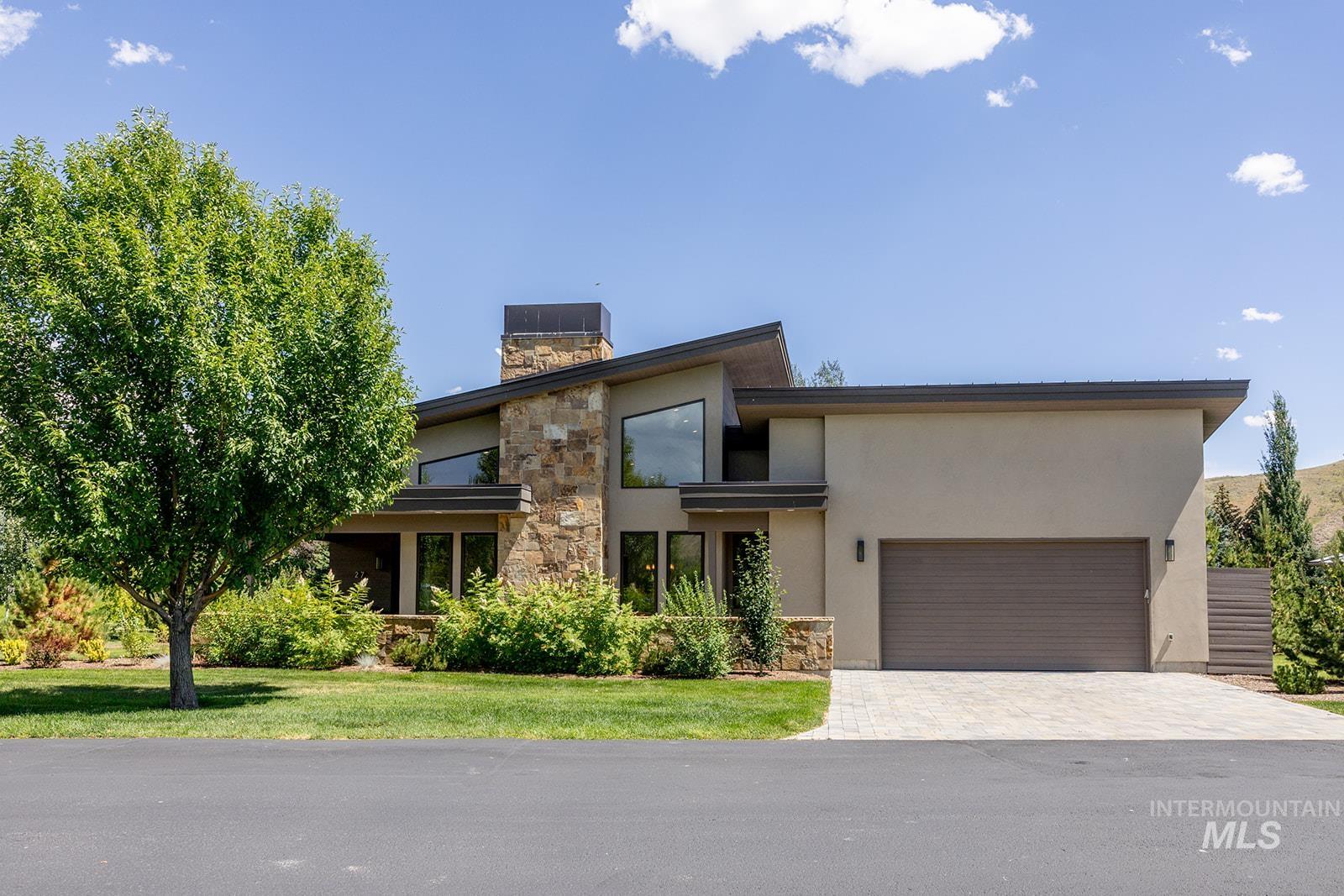 Contemporary house with stucco siding, an attached garage, stone siding, decorative driveway, and a chimney