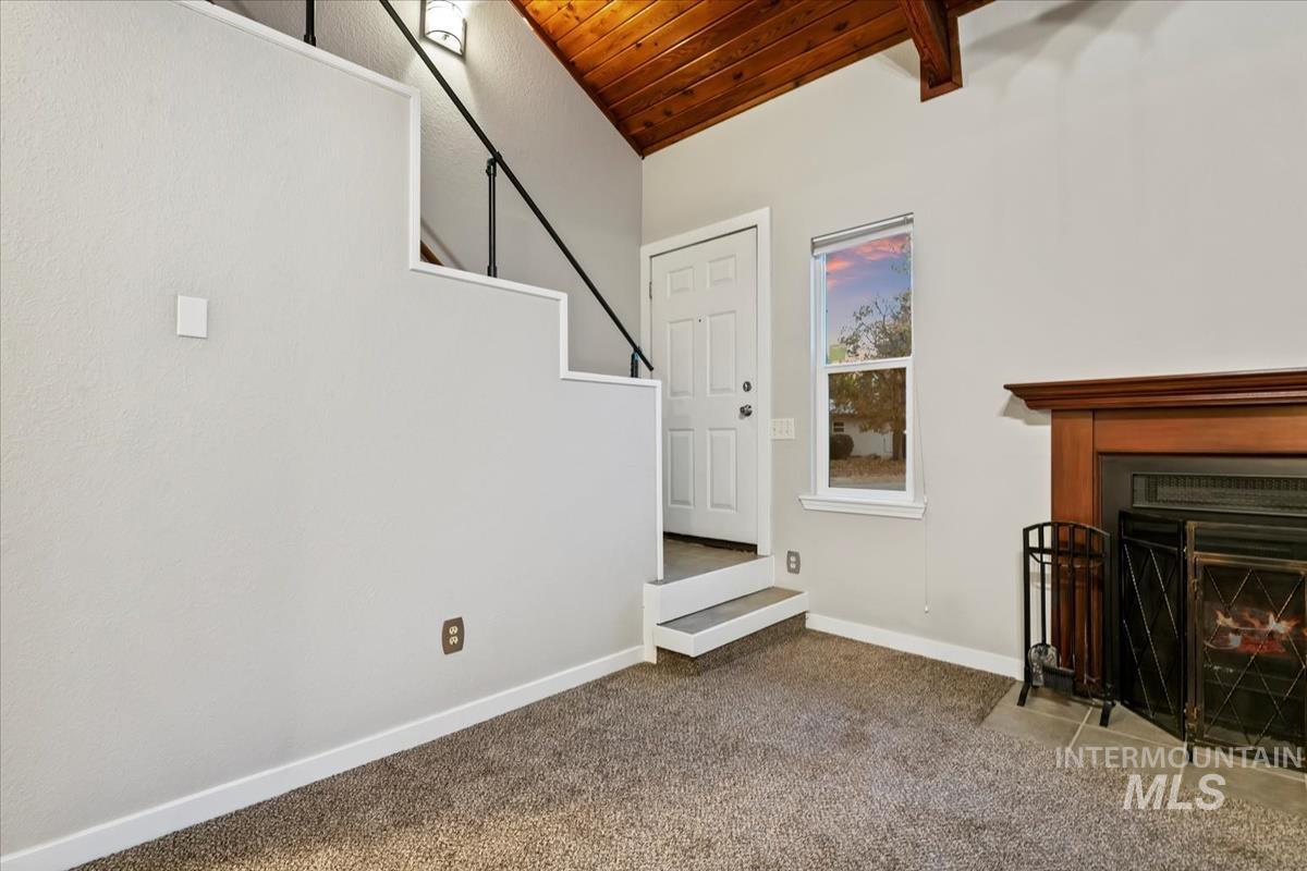 Carpeted living area with wood ceiling, a fireplace with flush hearth, stairs, and lofted ceiling