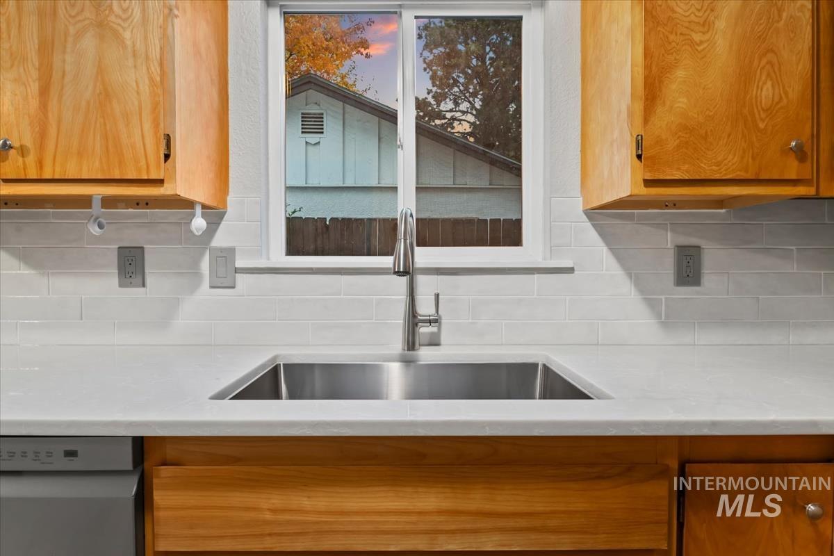 Kitchen featuring brown cabinets, dishwasher, light stone countertops, and tasteful backsplash