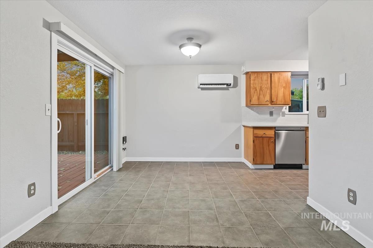 Kitchen with light countertops, stainless steel dishwasher, brown cabinets, light tile patterned floors, and a wall mounted air conditioner
