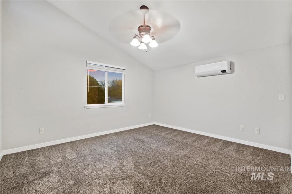 Spare room with lofted ceiling, dark colored carpet, a ceiling fan, and a wall mounted air conditioner